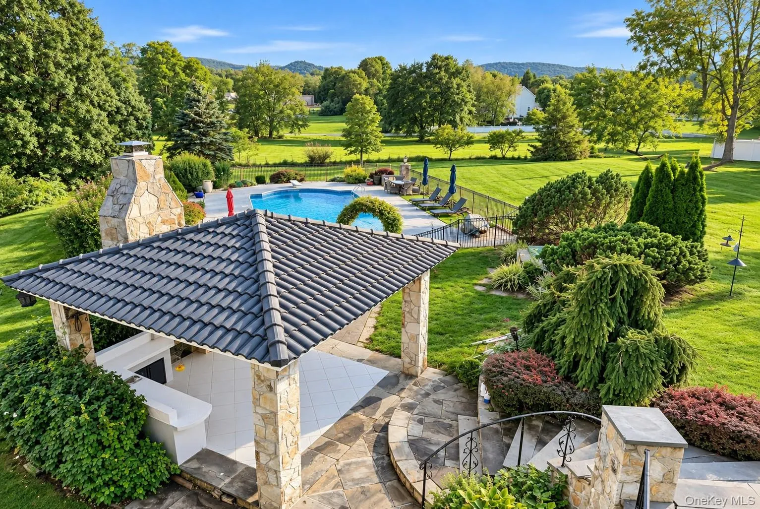 Expansive outdoor living area featuring a swimming pool, stone patio, stone fireplace, and a covered outdoor kitchen Expansive outdoor living area featuring a swimming pool, stone patio, stone fireplace, and a covered outdoor kitchen