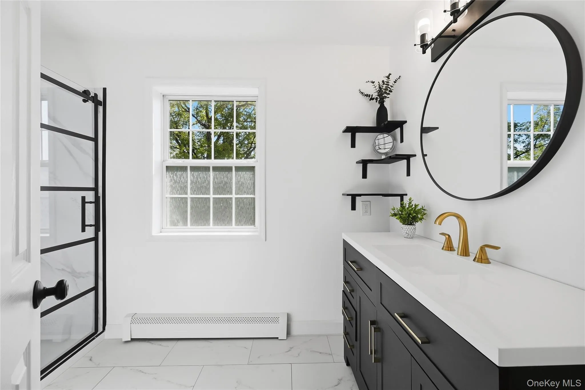Black-framed glass shower enclosure, single vanity with a white countertop and gold-toned faucet, large round mirror, and tile flooring Black-framed glass shower enclosure, single vanity with a white countertop and gold-toned faucet, large round mirror, and tile flooring