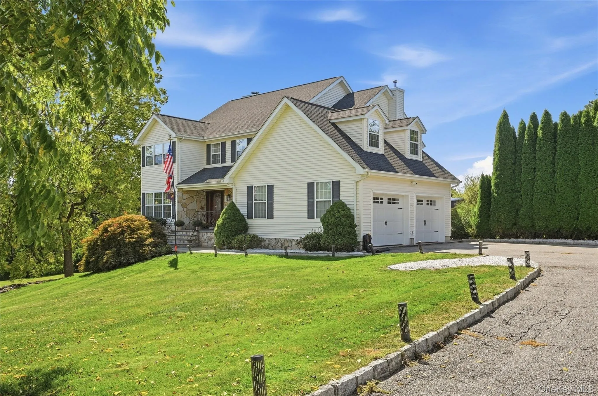 Two-story residence with dormer windows, stone facade accents, a multi-car garage, and mature landscaping Two-story residence with dormer windows, stone facade accents, a multi-car garage, and mature landscaping