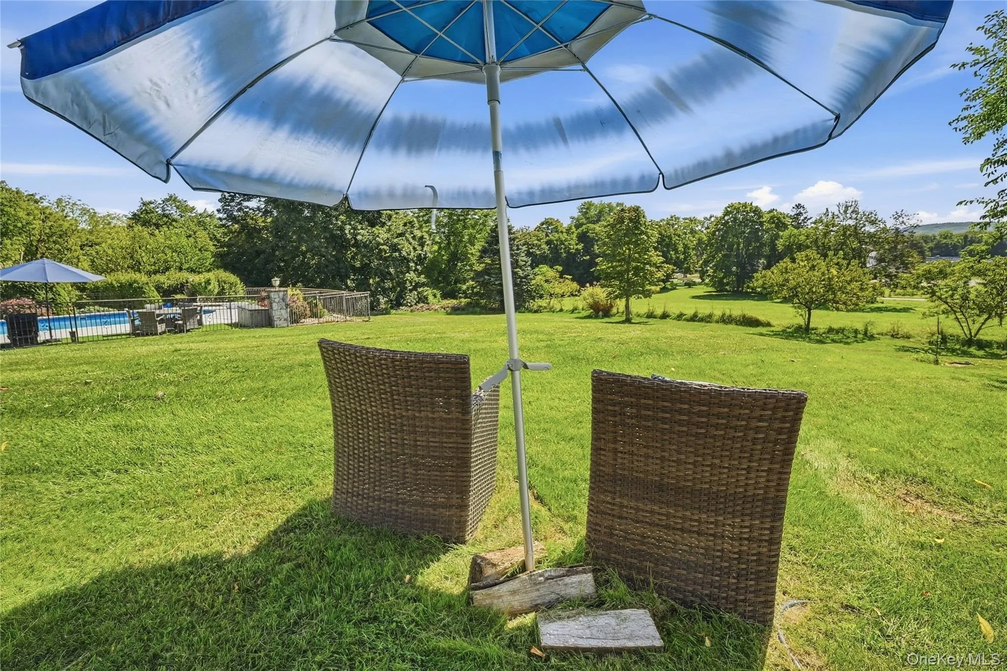 Expansive green lawn with mature trees and a fenced-in inground pool Expansive green lawn with mature trees and a fenced-in inground pool