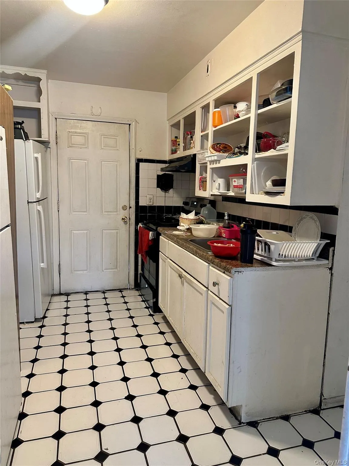 Kitchen with freestanding refrigerator, black range with electric cooktop, dark countertops, light floors, and tasteful backsplash Kitchen with freestanding refrigerator, black range with electric cooktop, dark countertops, light floors, and tasteful backsplash