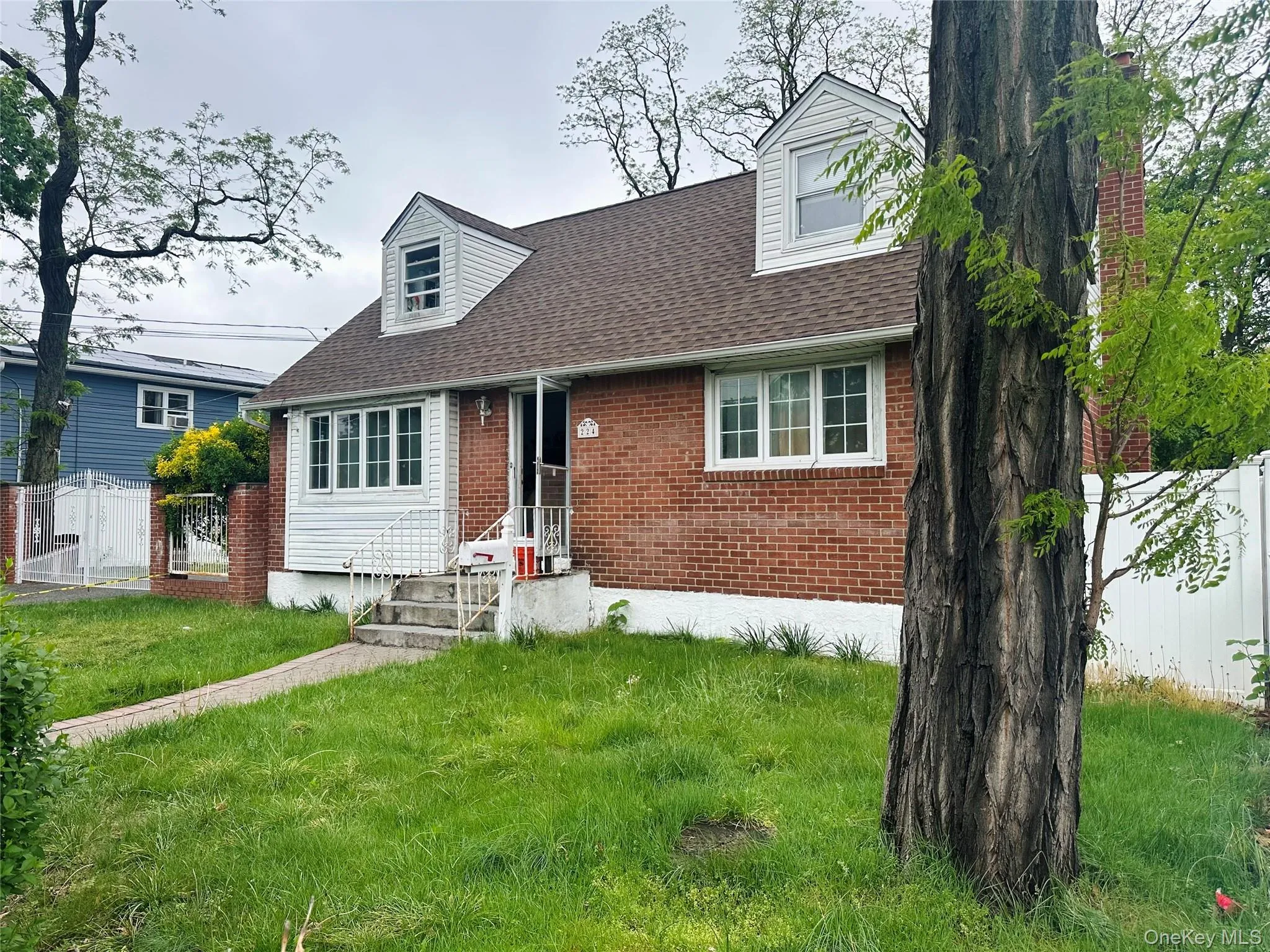New england style home featuring roof with shingles, fence, a front lawn, and brick siding New england style home featuring roof with shingles, fence, a front lawn, and brick siding