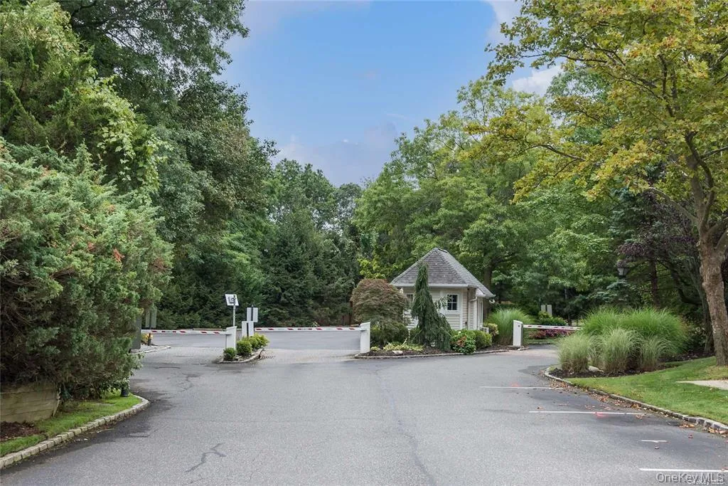 Gated entrance featuring a guardhouse with a shingled roof, automated access barriers, and mature landscaping Gated entrance featuring a guardhouse with a shingled roof, automated access barriers, and mature landscaping