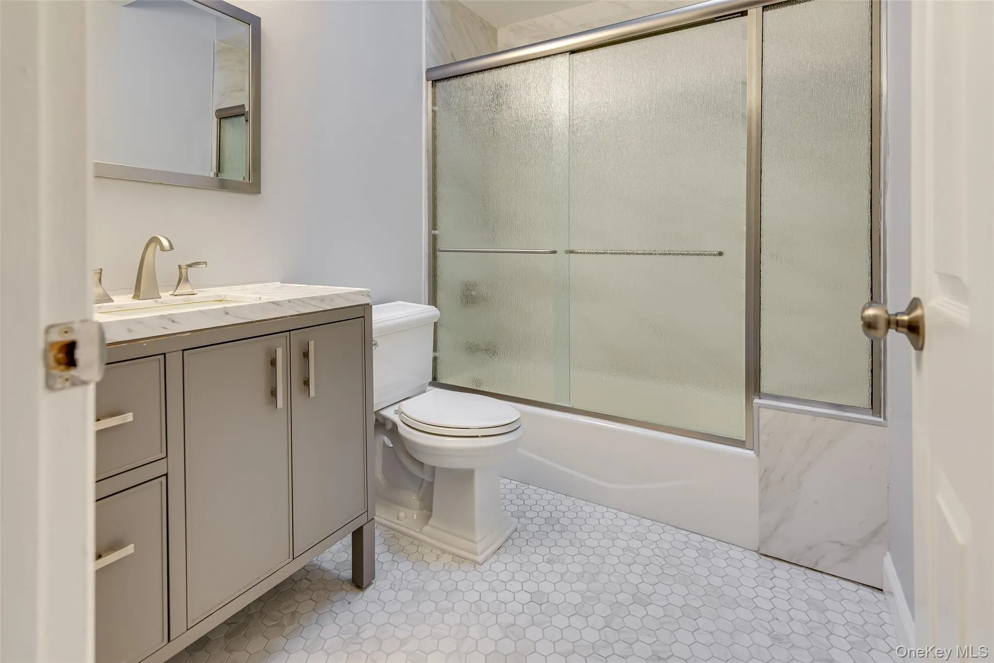 Bathroom featuring a single vanity with a solid surface countertop, brushed nickel faucet, framed wall mirror, and hexagonal floor tiling Bathroom featuring a single vanity with a solid surface countertop, brushed nickel faucet, framed wall mirror, and hexagonal floor tiling