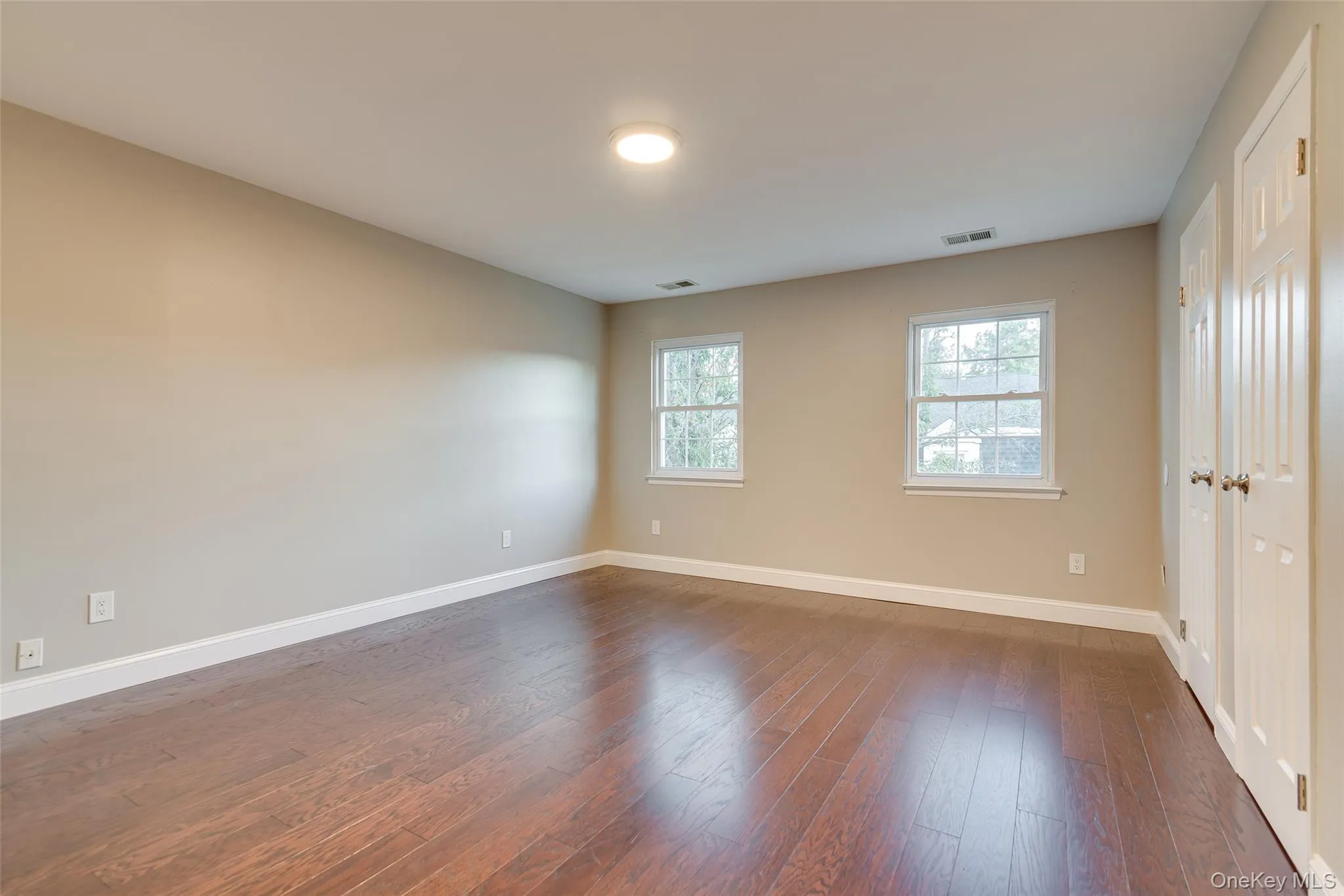 Wood-finish flooring, neutral wall tones, two windows with white trim, white baseboards, and white paneled bi-fold closet doors Wood-finish flooring, neutral wall tones, two windows with white trim, white baseboards, and white paneled bi-fold closet doors