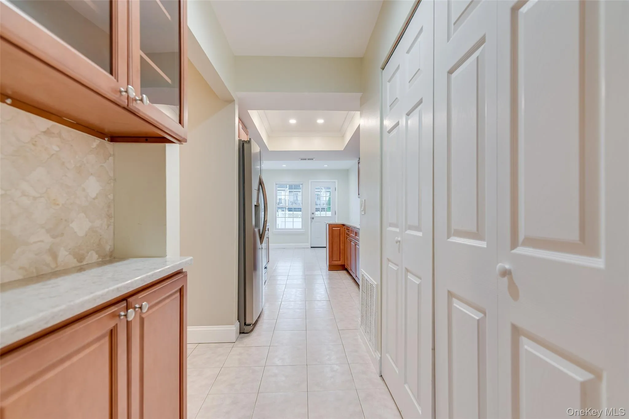 Built-in cabinetry with glass-front uppers, light-toned countertop, and patterned backsplash Built-in cabinetry with glass-front uppers, light-toned countertop, and patterned backsplash