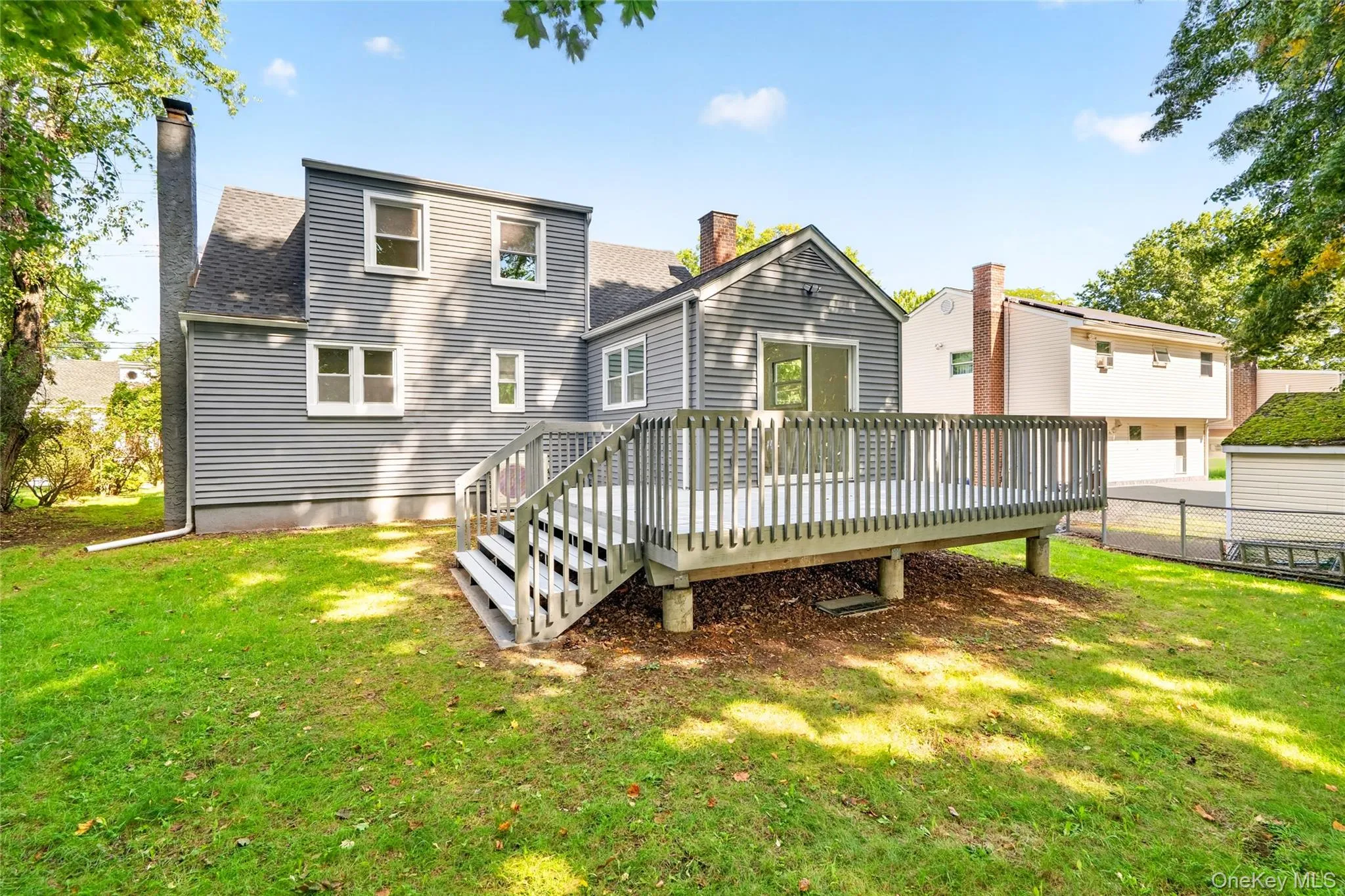 Expansive backyard with a large wooden deck featuring a sliding glass door, a detached shed, and a chain-link fence Expansive backyard with a large wooden deck featuring a sliding glass door, a detached shed, and a chain-link fence