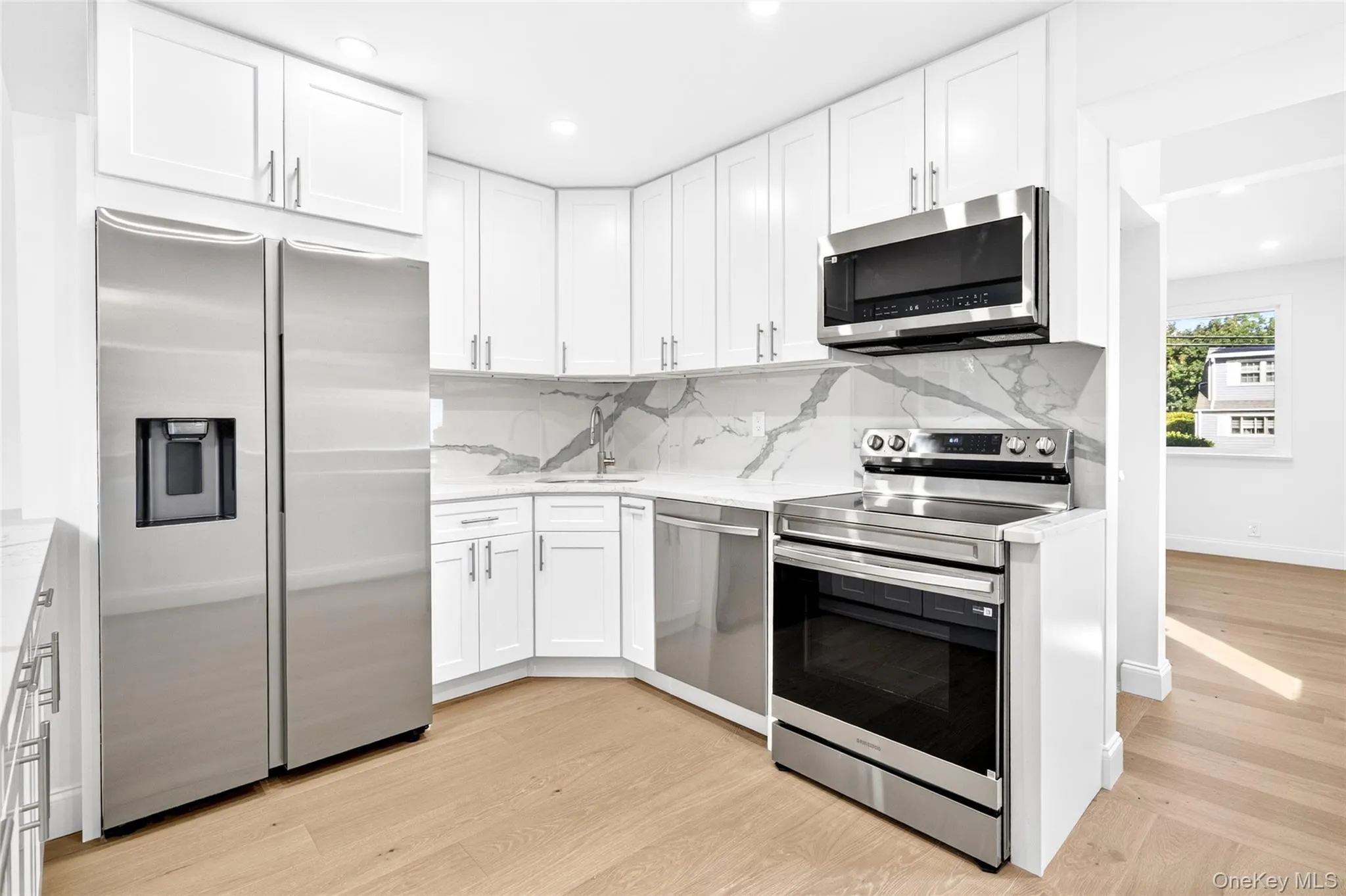 White shaker cabinetry, stainless steel appliances, light wood-finish flooring, and white countertops with a patterned backsplash White shaker cabinetry, stainless steel appliances, light wood-finish flooring, and white countertops with a patterned backsplash