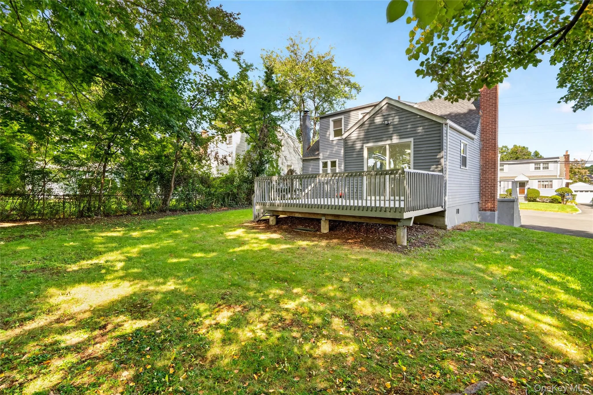 Expansive rear yard featuring a wooden deck, mature trees, and a brick chimney Expansive rear yard featuring a wooden deck, mature trees, and a brick chimney