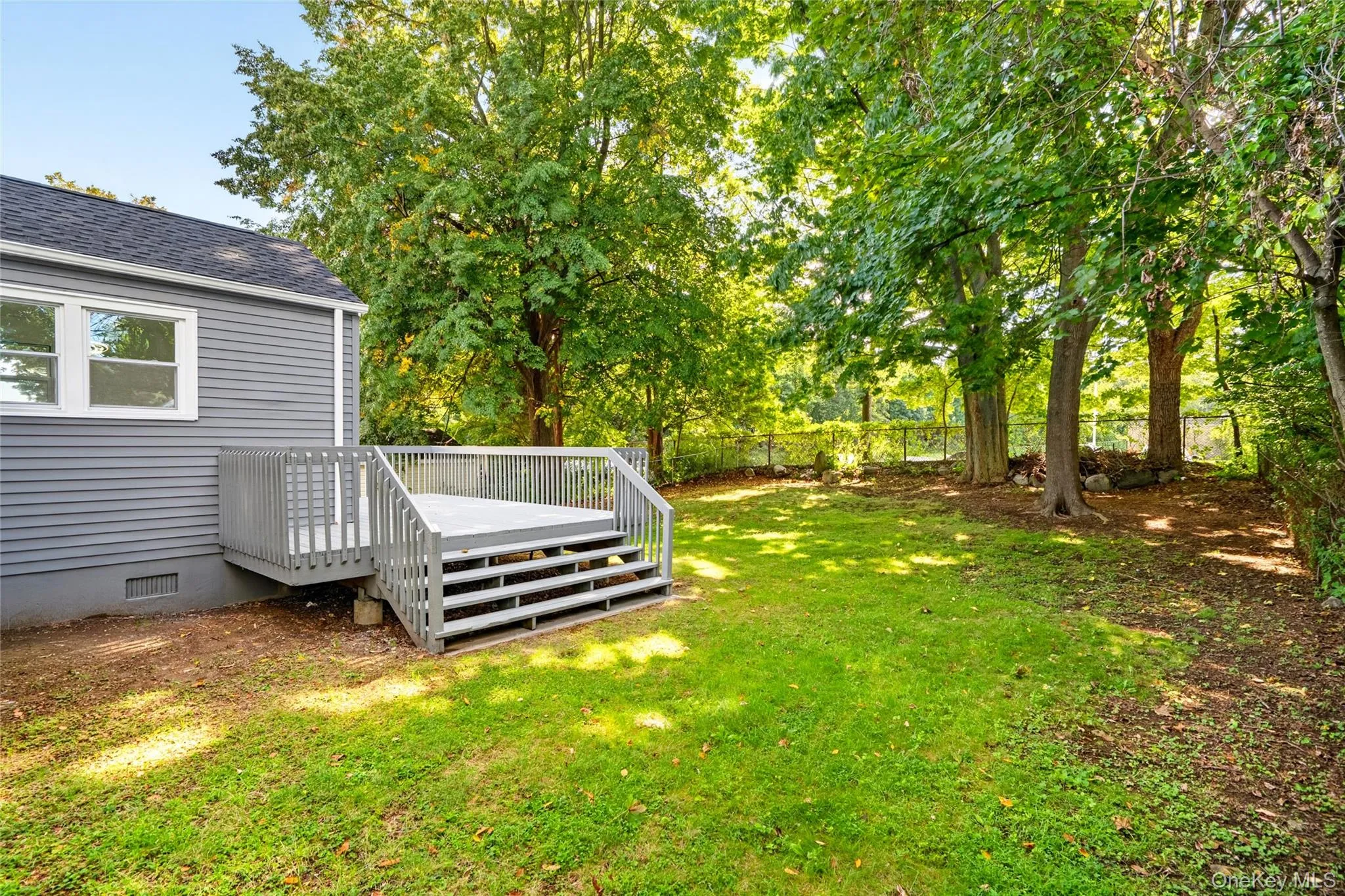 Expansive grassy yard with mature trees, a deck, and gray siding Expansive grassy yard with mature trees, a deck, and gray siding