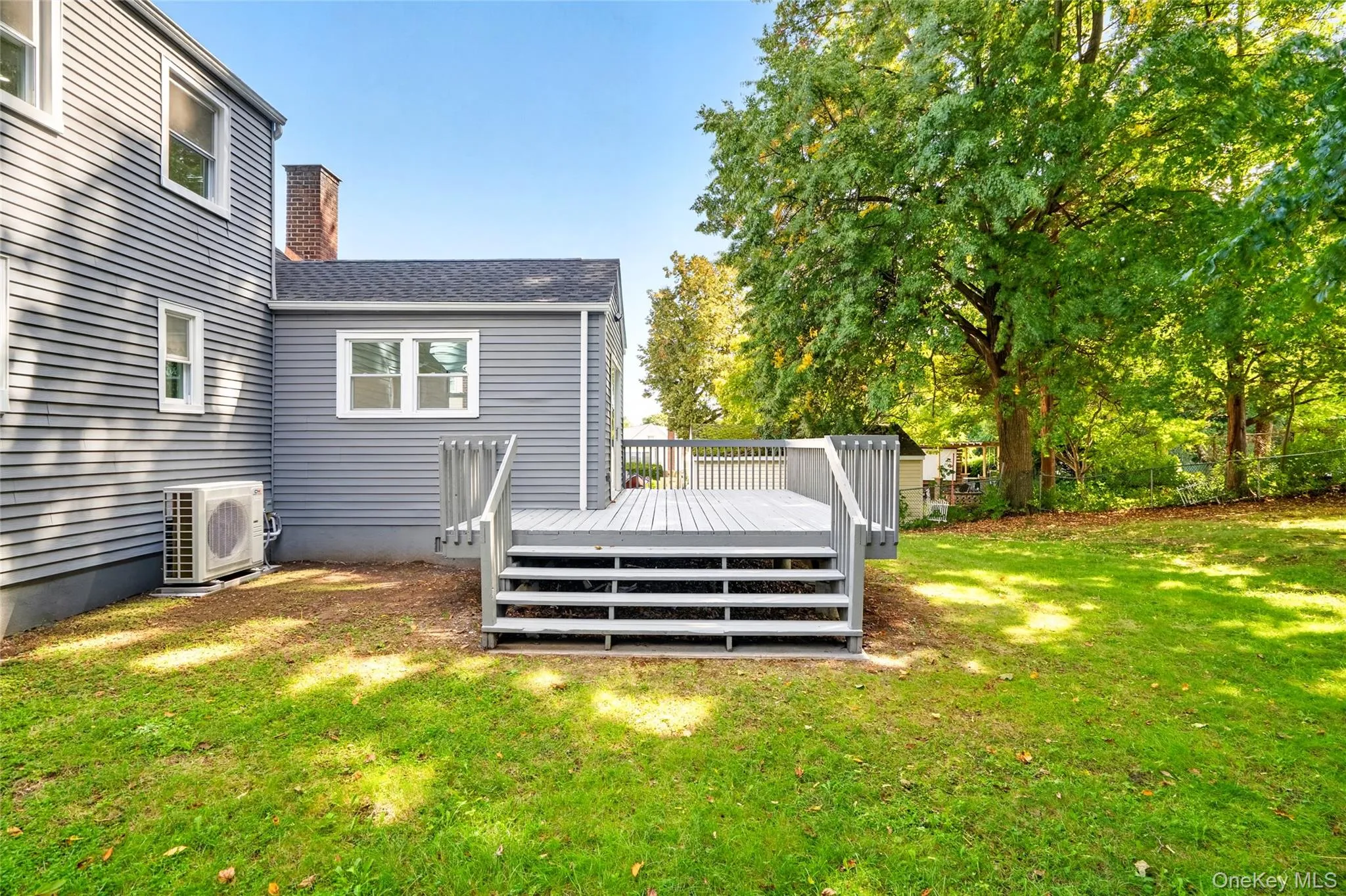 Expansive backyard featuring a manicured lawn, mature trees, and a deck with steps Expansive backyard featuring a manicured lawn, mature trees, and a deck with steps