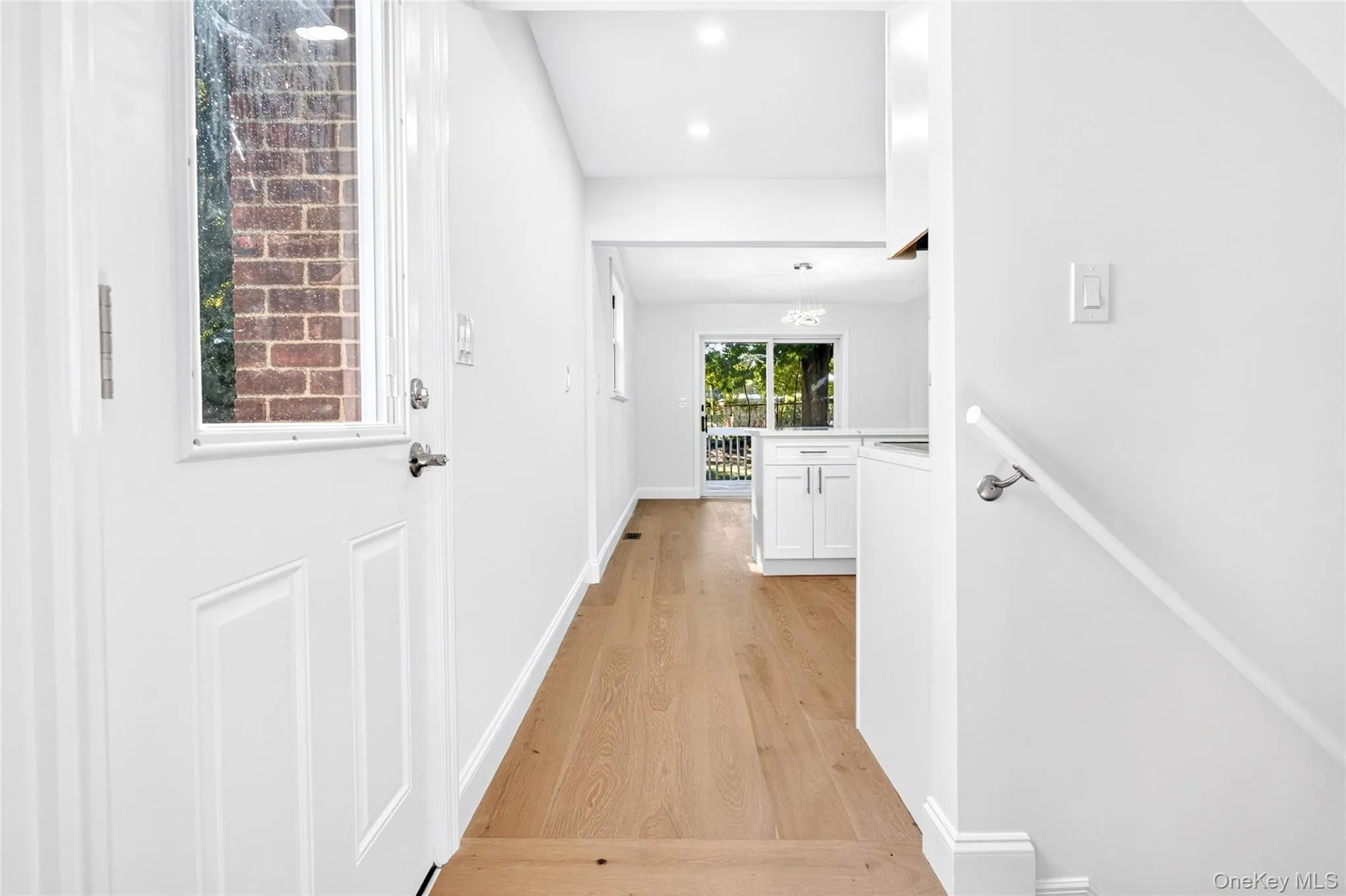 Bright entryway with wood-finish flooring, white paneled door with window, and a white handrail Bright entryway with wood-finish flooring, white paneled door with window, and a white handrail