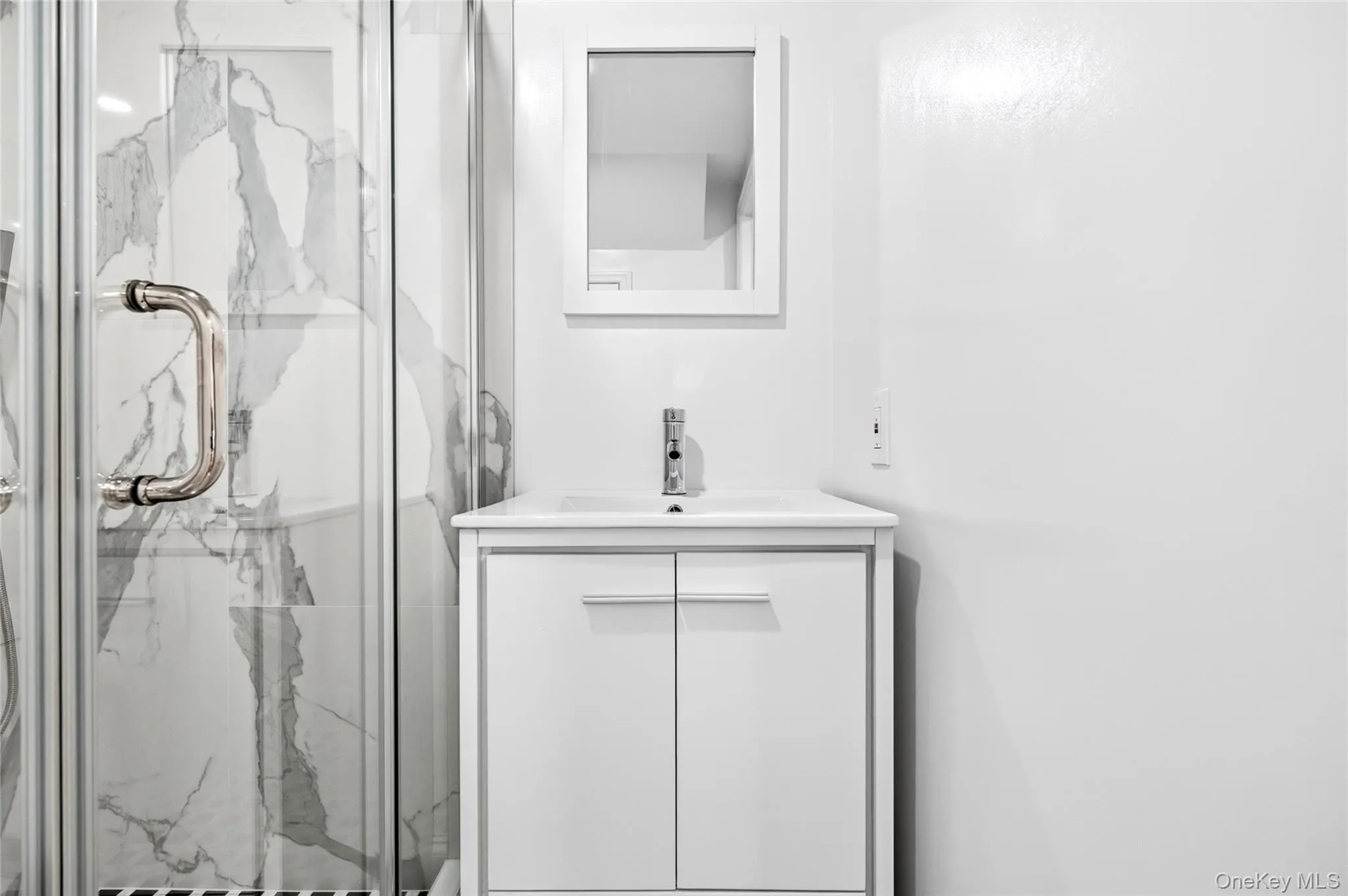Glass-enclosed shower with a polished chrome handle, white marble-look shower surround, white vanity, and chrome faucet Glass-enclosed shower with a polished chrome handle, white marble-look shower surround, white vanity, and chrome faucet