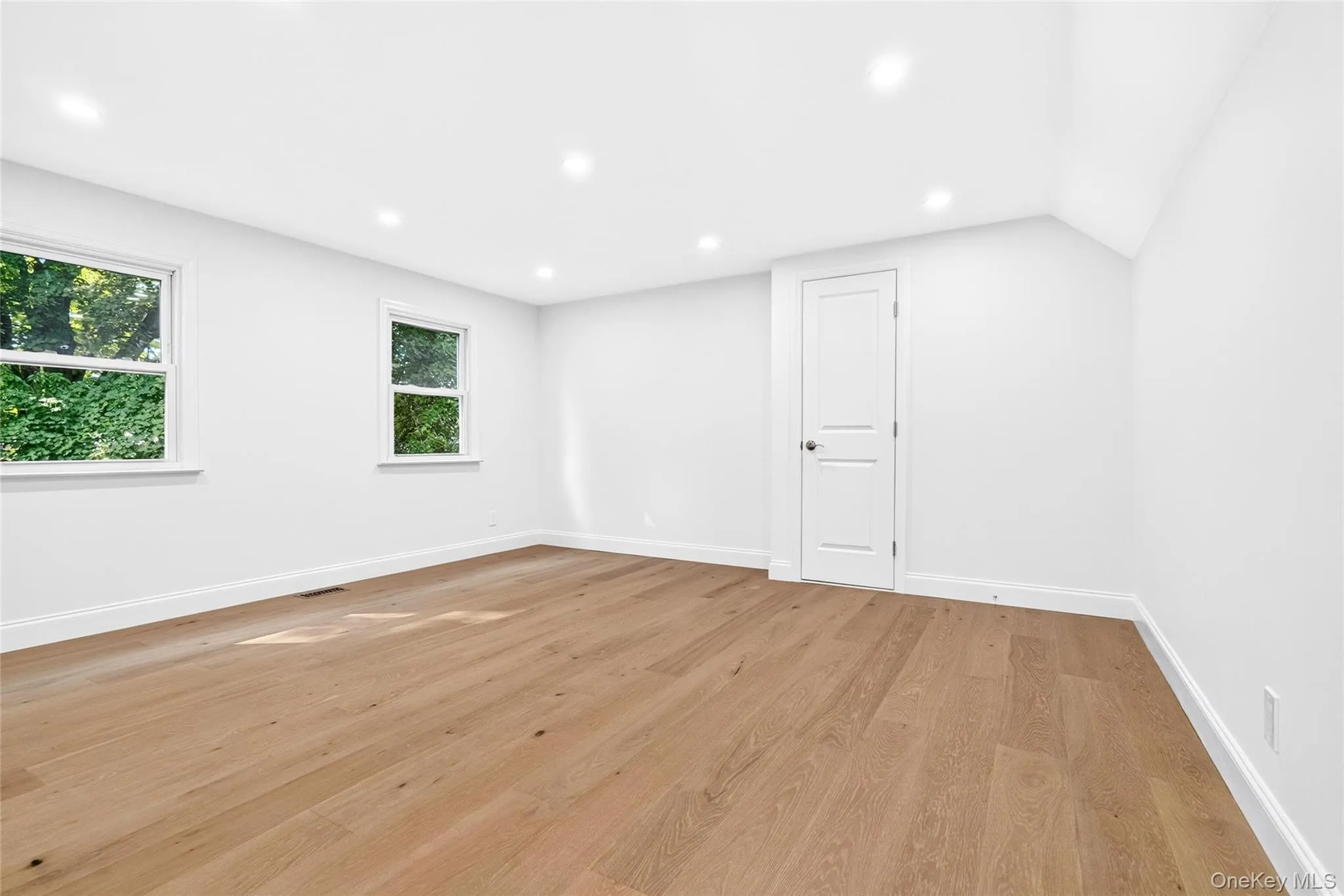 Recessed ceiling lighting, wood-finish flooring, two windows with white trim, white paneled door, and white painted walls Recessed ceiling lighting, wood-finish flooring, two windows with white trim, white paneled door, and white painted walls