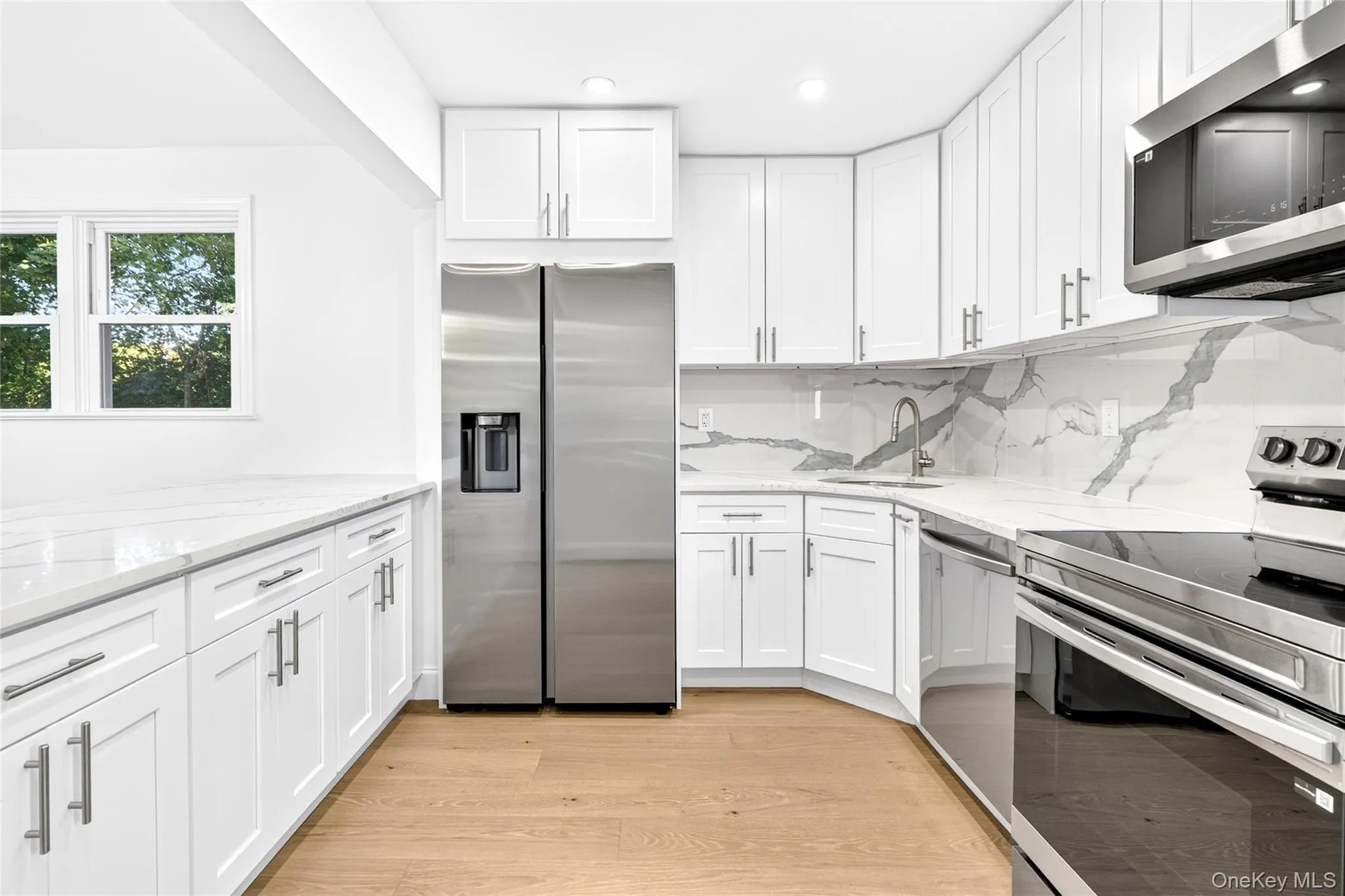 White shaker cabinetry, stainless steel appliances, wood-finish flooring, white countertop, and patterned backsplash White shaker cabinetry, stainless steel appliances, wood-finish flooring, white countertop, and patterned backsplash