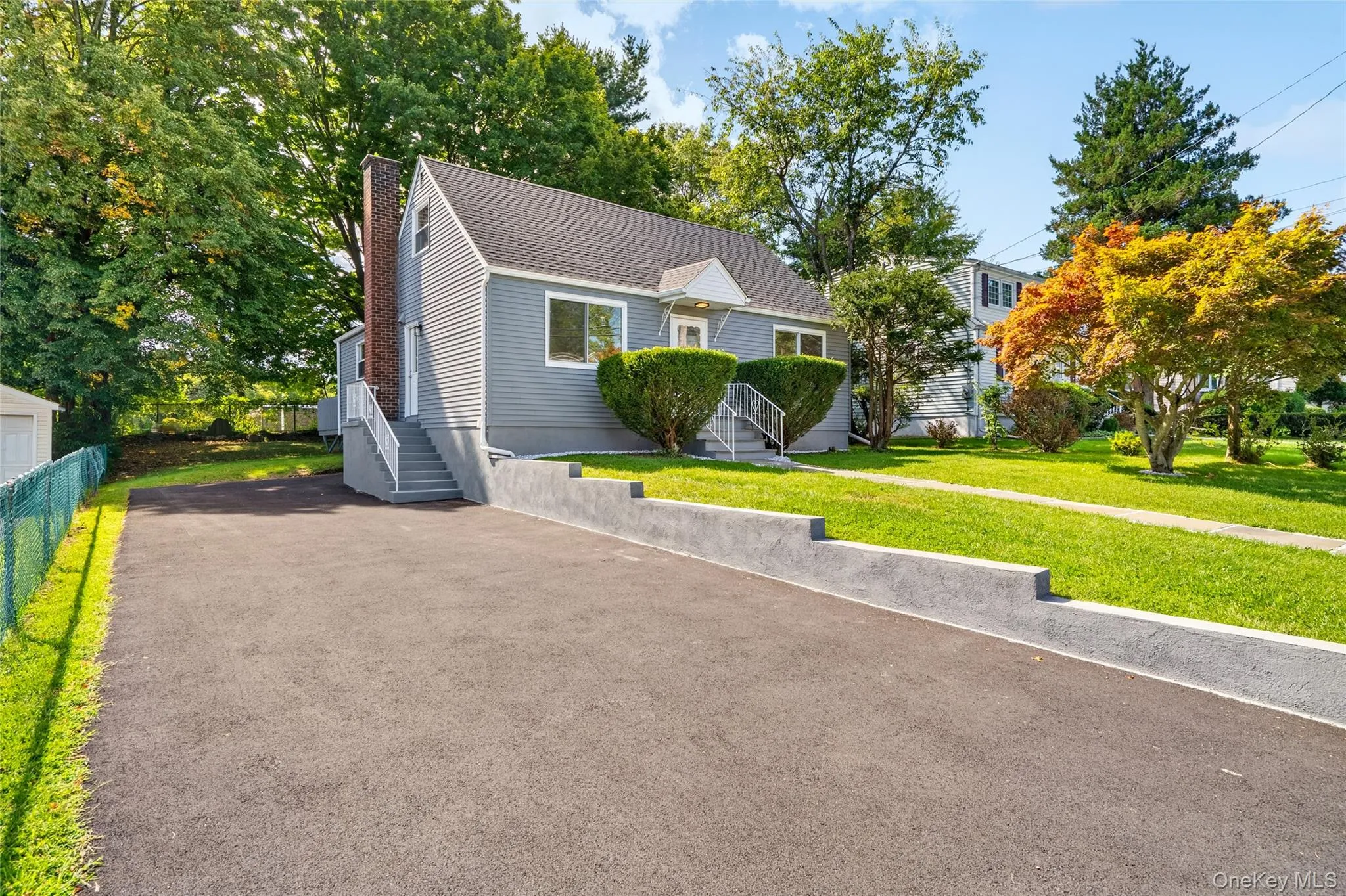 Exterior featuring gray vinyl siding, a dark roof, a concrete retaining wall, and a paved driveway Exterior featuring gray vinyl siding, a dark roof, a concrete retaining wall, and a paved driveway