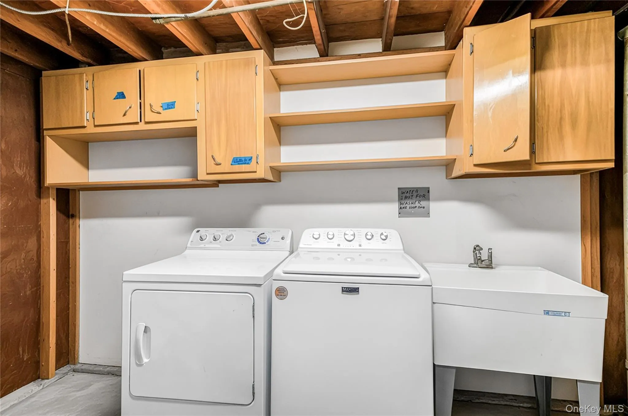 Utility room with exposed ceiling joists, light wood-finish cabinetry, open shelving, and a utility sink Utility room with exposed ceiling joists, light wood-finish cabinetry, open shelving, and a utility sink