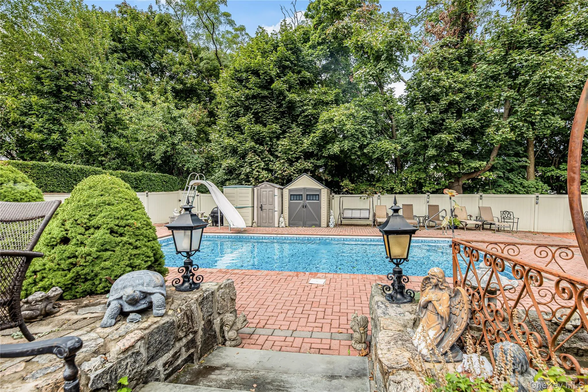 Swimming pool with a water slide, surrounded by a brick paver patio and privacy fencing Swimming pool with a water slide, surrounded by a brick paver patio and privacy fencing