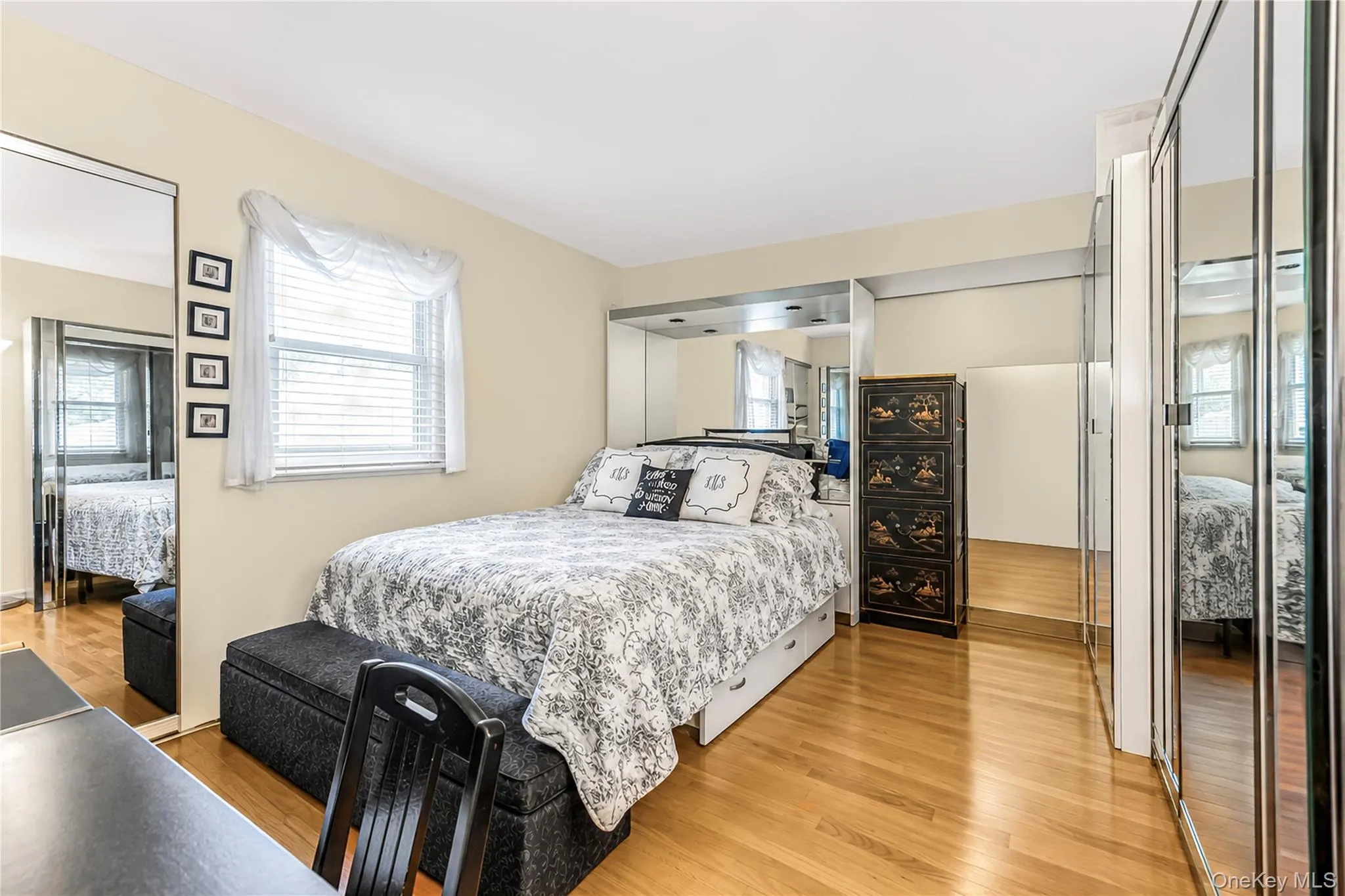 Hardwood flooring, mirrored closet doors, a built-in mirrored headboard, and a window with blinds Hardwood flooring, mirrored closet doors, a built-in mirrored headboard, and a window with blinds
