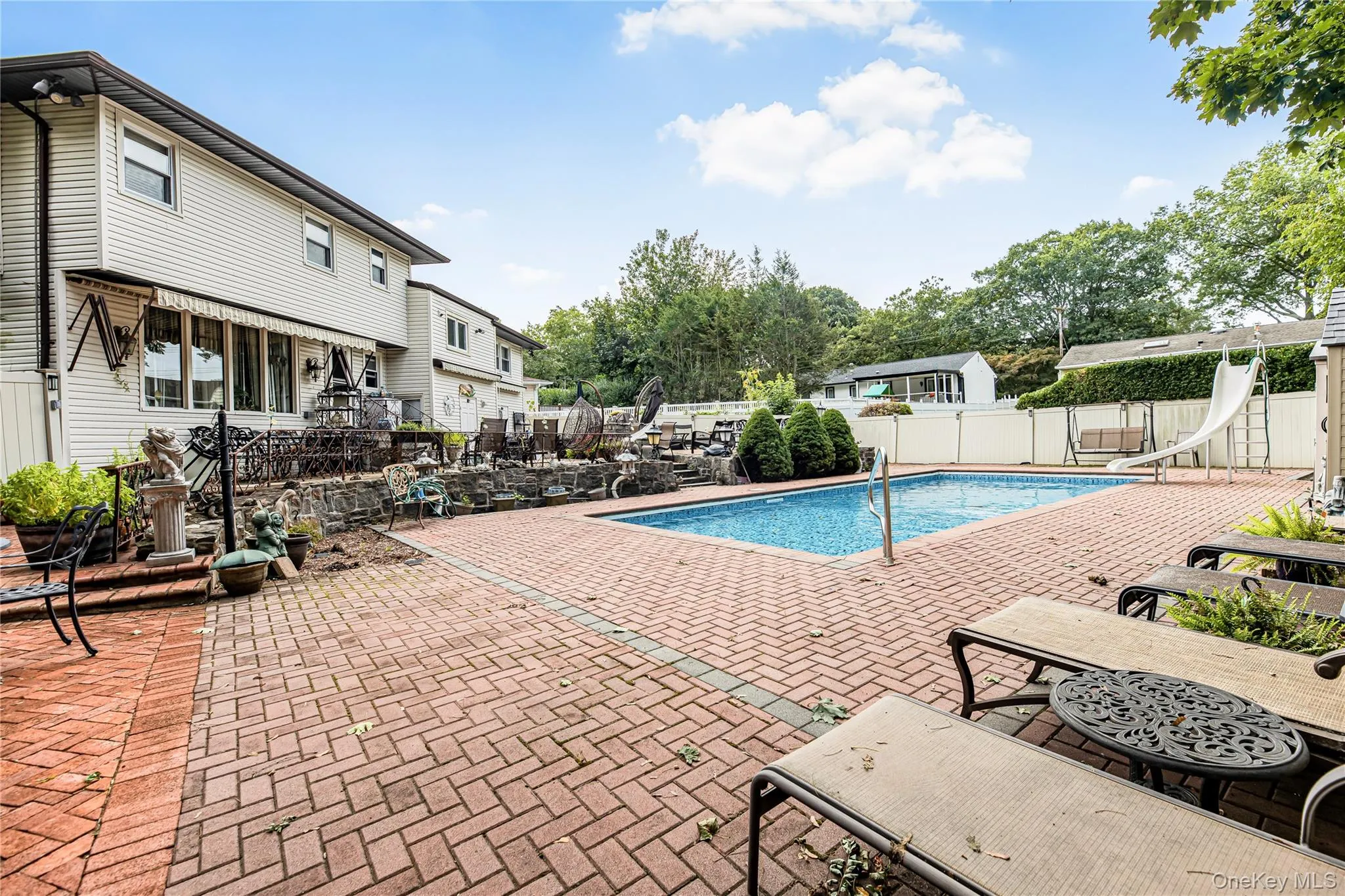 Swimming pool with a water slide, surrounded by a brick paver patio and privacy fencing Swimming pool with a water slide, surrounded by a brick paver patio and privacy fencing
