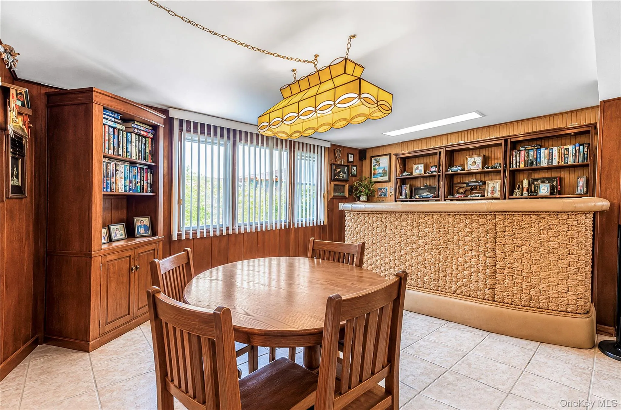 Wood-paneled room featuring extensive built-in shelving, a patterned bar with a built-in display, and tiled flooring Wood-paneled room featuring extensive built-in shelving, a patterned bar with a built-in display, and tiled flooring