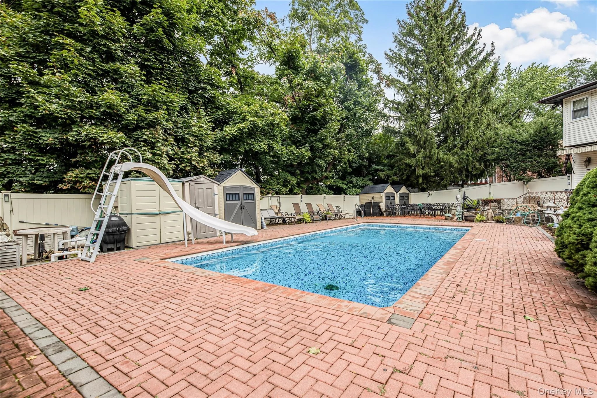 Swimming pool with a water slide, surrounded by a brick paver patio and privacy fencing Swimming pool with a water slide, surrounded by a brick paver patio and privacy fencing