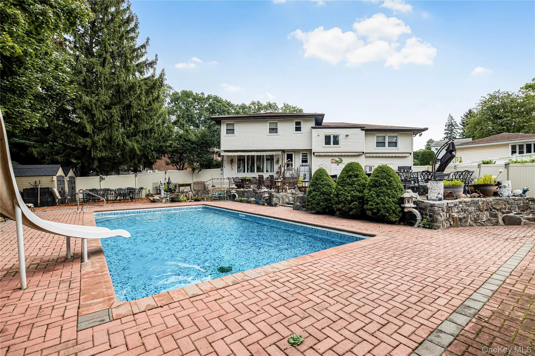 Swimming pool with a water slide, surrounded by a brick paver patio and privacy fencing Swimming pool with a water slide, surrounded by a brick paver patio and privacy fencing
