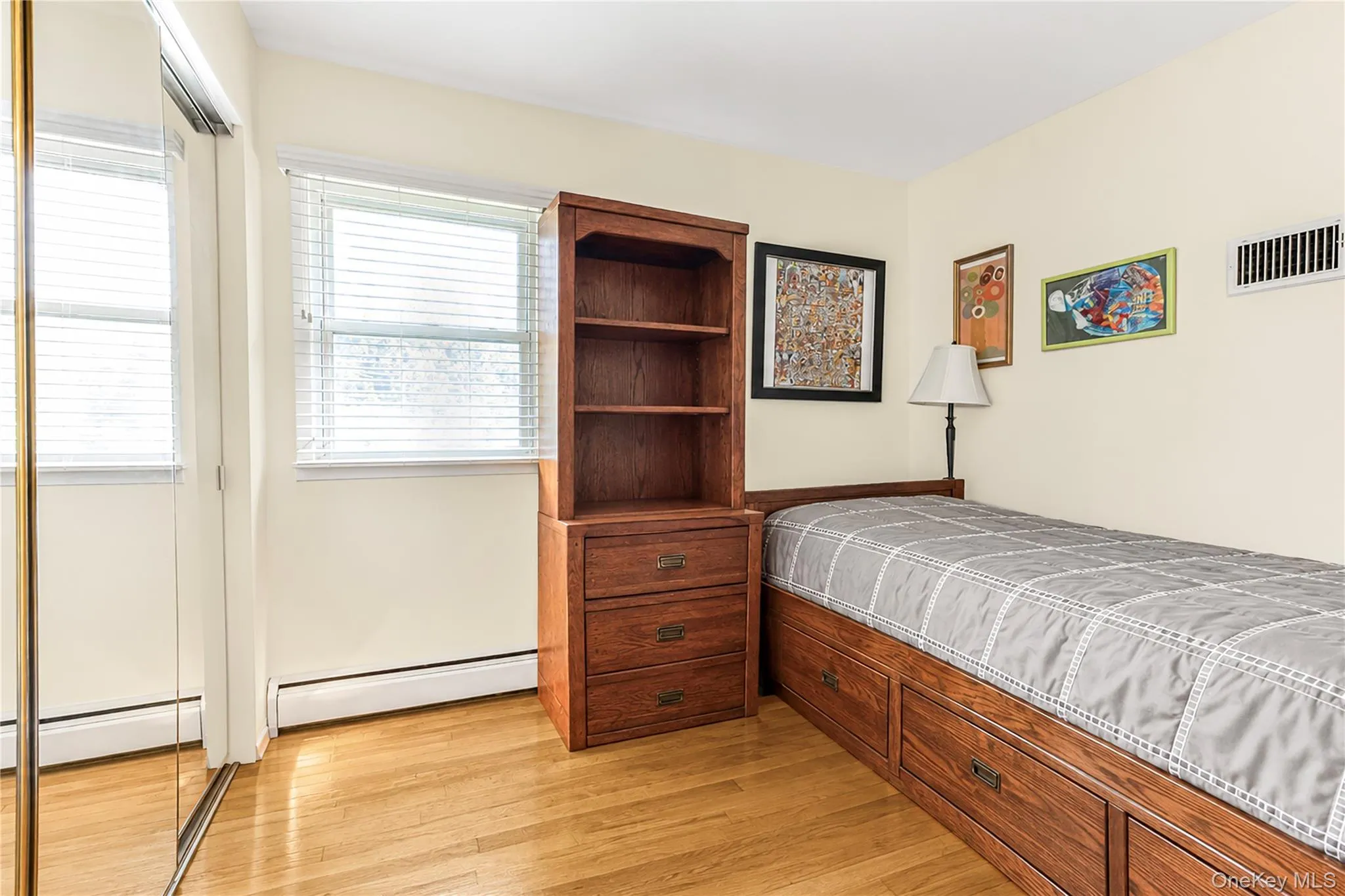 Bright interior with light wood-finish flooring, a window offering natural illumination, and mirrored closet doors Bright interior with light wood-finish flooring, a window offering natural illumination, and mirrored closet doors