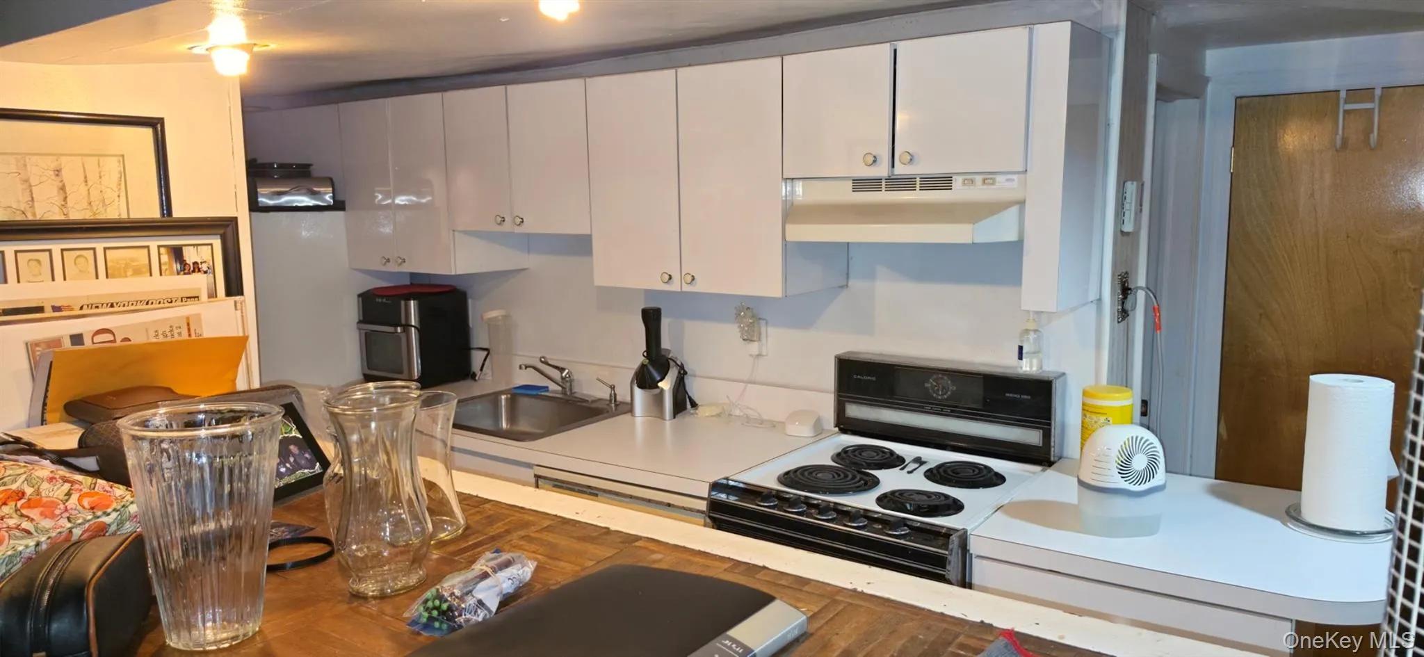 Kitchen featuring white cabinetry, a stainless steel sink, an electric range, and a white countertop Kitchen featuring white cabinetry, a stainless steel sink, an electric range, and a white countertop