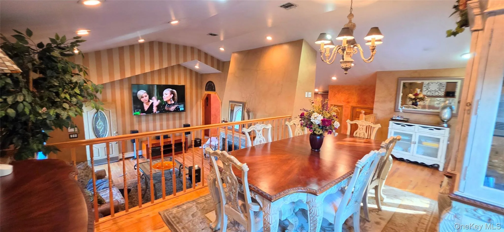 Vaulted ceiling featuring recessed lighting, striped wall treatment, wood-finish flooring, metal spindle railing, and a tiered chandelier Vaulted ceiling featuring recessed lighting, striped wall treatment, wood-finish flooring, metal spindle railing, and a tiered chandelier