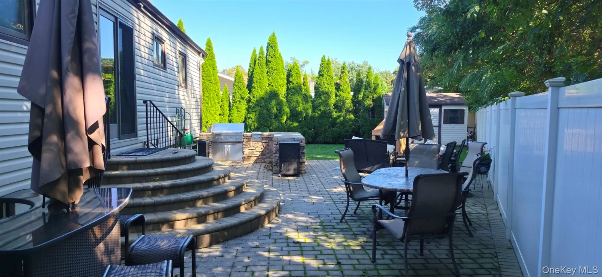 Expansive paver patio with a built-in outdoor kitchen, stone retaining wall, and curved stone steps leading to a sliding glass door Expansive paver patio with a built-in outdoor kitchen, stone retaining wall, and curved stone steps leading to a sliding glass door