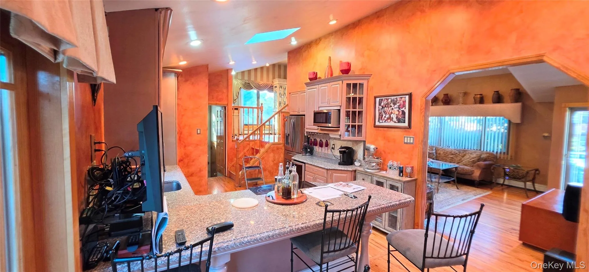 Kitchen featuring a stone-surface breakfast bar, wood-finish cabinetry with integrated display shelving, vaulted ceiling with a skylight, and recessed lighting Kitchen featuring a stone-surface breakfast bar, wood-finish cabinetry with integrated display shelving, vaulted ceiling with a skylight, and recessed lighting