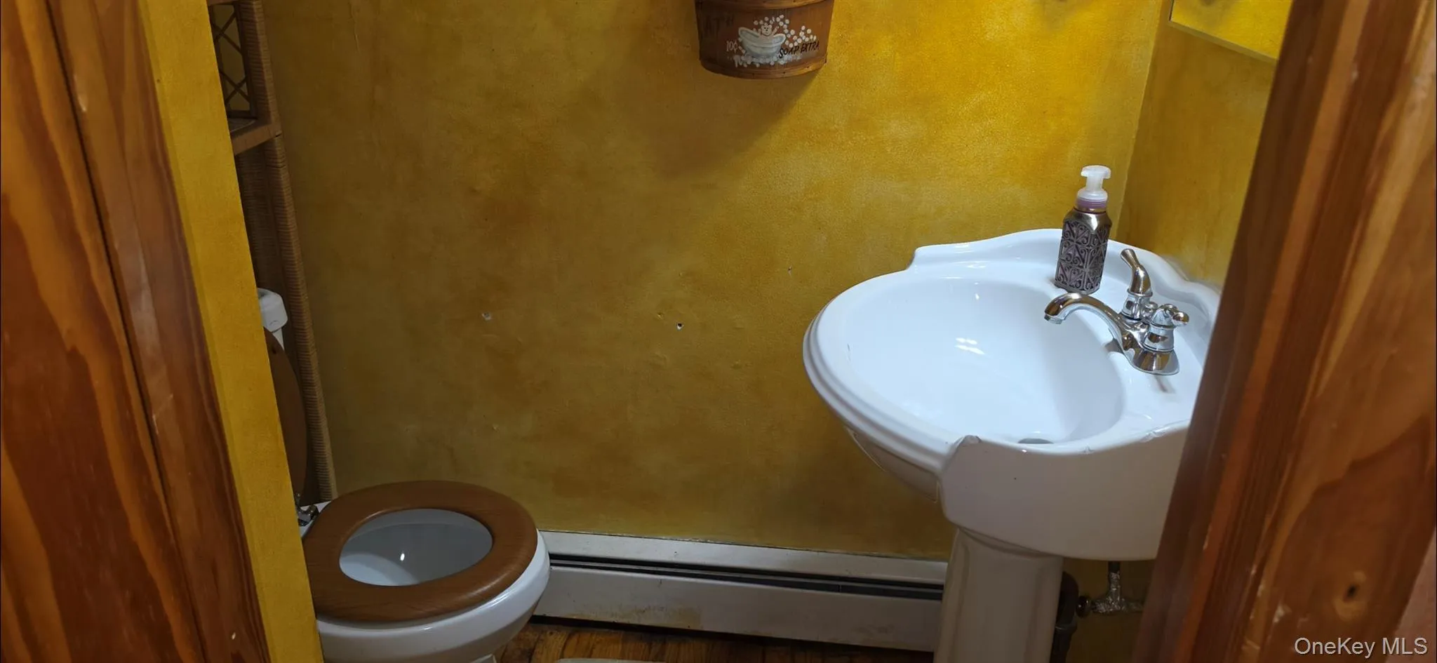 Pedestal sink with chrome fixtures, white toilet with wood-finish seat, and textured yellow wall finish Pedestal sink with chrome fixtures, white toilet with wood-finish seat, and textured yellow wall finish