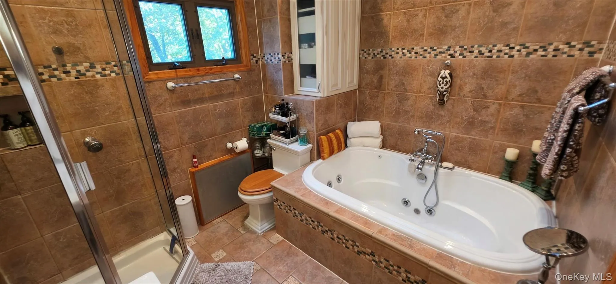 Bathroom featuring a jetted soaking tub with chrome-finish faucet, separate glass-enclosed shower, tile-surround walls with decorative inlay, and built-in cabinetry Bathroom featuring a jetted soaking tub with chrome-finish faucet, separate glass-enclosed shower, tile-surround walls with decorative inlay, and built-in cabinetry