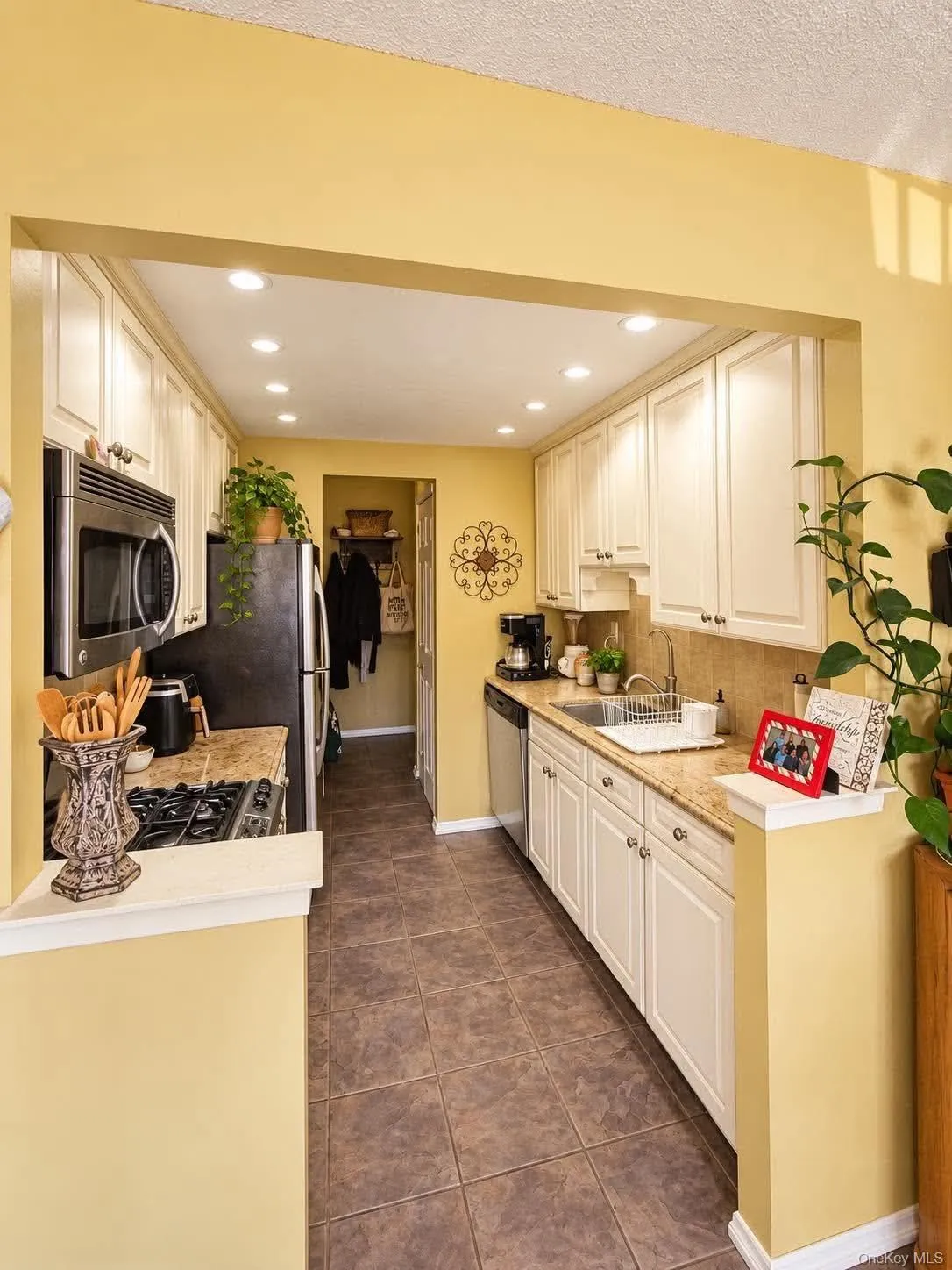 Kitchen with recessed lighting, white cabinetry, integrated stainless steel appliances, and brown tile flooring Kitchen with recessed lighting, white cabinetry, integrated stainless steel appliances, and brown tile flooring
