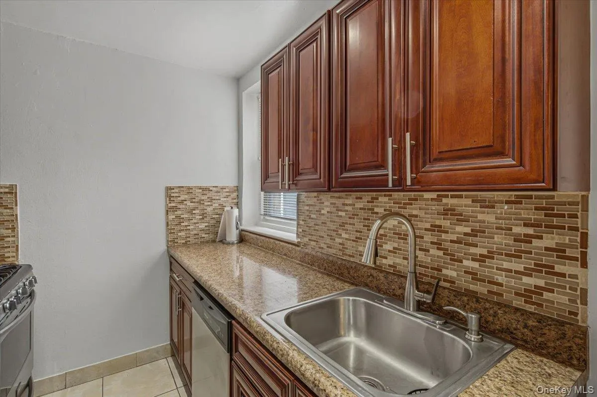 Kitchen featuring wood cabinetry, a stainless steel sink with a high-arch faucet, granite-finish countertops, and a mosaic tile backsplash Kitchen featuring wood cabinetry, a stainless steel sink with a high-arch faucet, granite-finish countertops, and a mosaic tile backsplash