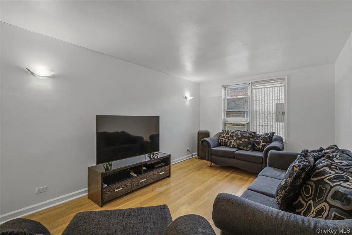 Wood-finish flooring with white baseboards, wall-mounted sconce lighting, and a window with blinds Wood-finish flooring with white baseboards, wall-mounted sconce lighting, and a window with blinds