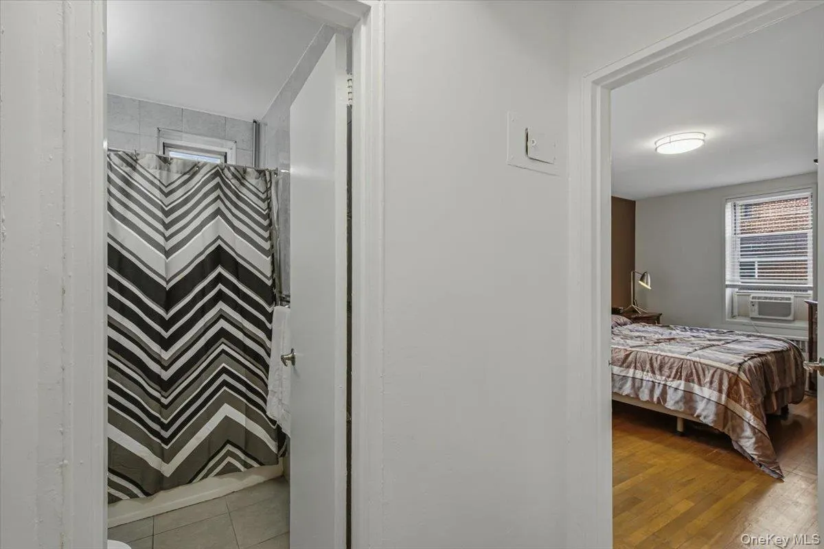 Bathroom featuring a tiled shower surround and a bedroom with wood-finish flooring and window blinds Bathroom featuring a tiled shower surround and a bedroom with wood-finish flooring and window blinds