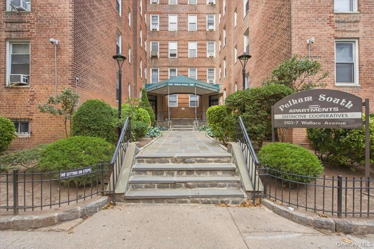 Brick building exterior featuring a stone walkway, landscaped shrubbery, and a covered entrance with a green awning Brick building exterior featuring a stone walkway, landscaped shrubbery, and a covered entrance with a green awning