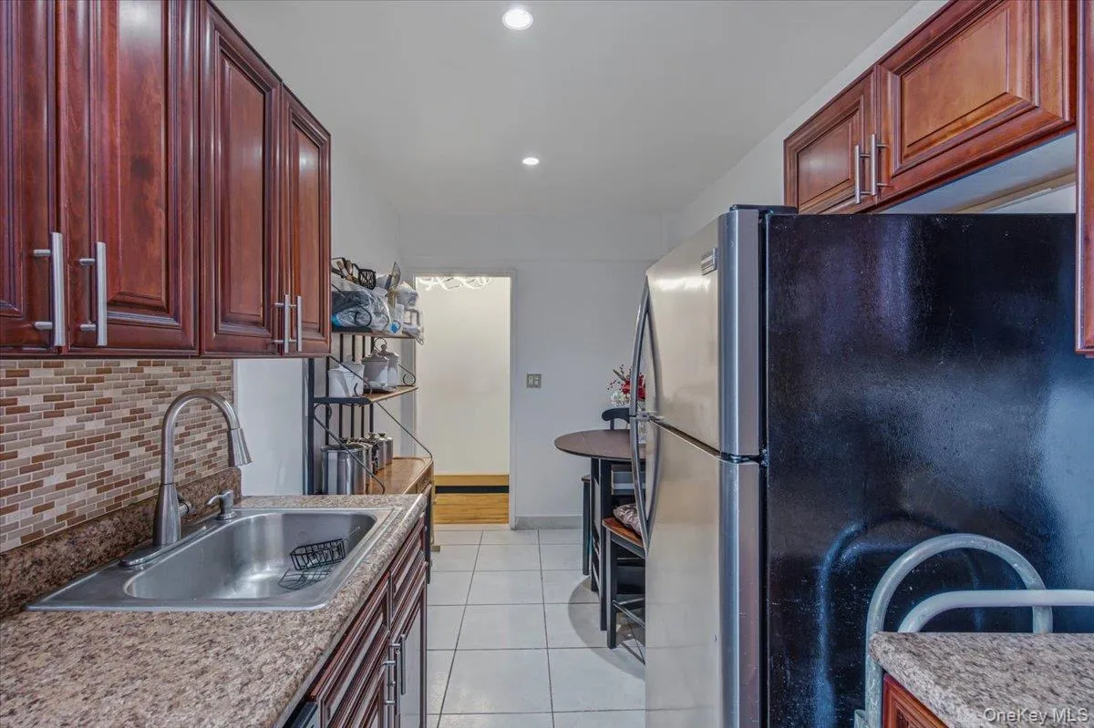 Galley kitchen featuring wood-finish cabinetry, granite-style countertops, stainless steel sink with pull-down faucet, and a mosaic tile backsplash Galley kitchen featuring wood-finish cabinetry, granite-style countertops, stainless steel sink with pull-down faucet, and a mosaic tile backsplash