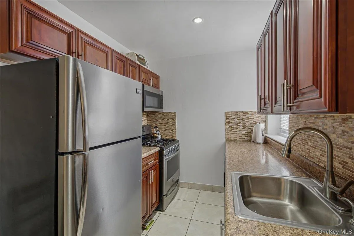 Kitchen featuring stainless steel appliances, wood-finish cabinetry, a stainless steel sink with gooseneck faucet, light-toned countertop, and mosaic tile backsplash Kitchen featuring stainless steel appliances, wood-finish cabinetry, a stainless steel sink with gooseneck faucet, light-toned countertop, and mosaic tile backsplash