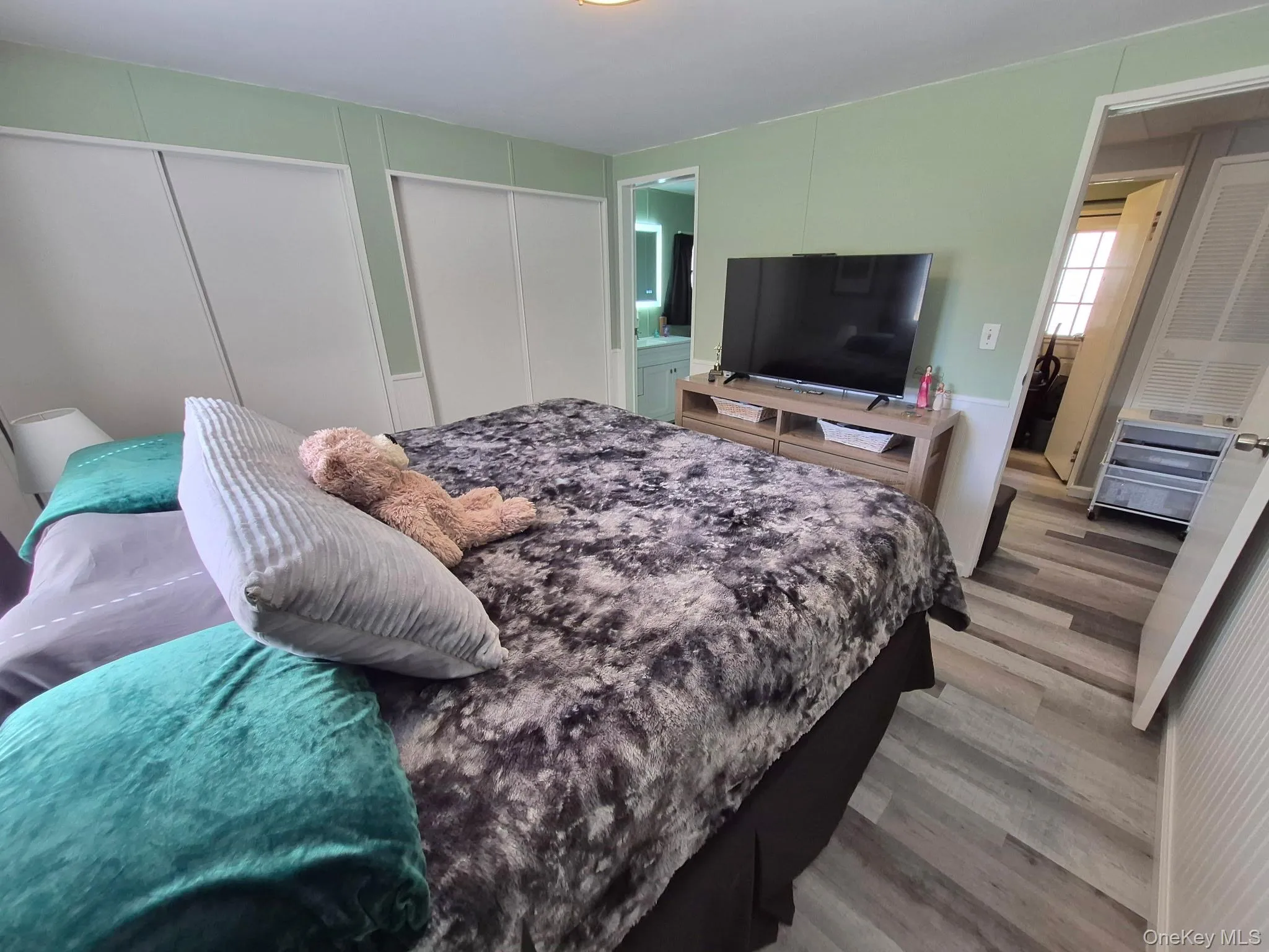 Wood-finish flooring throughout, with light green wall paneling, and white sliding closet doors Wood-finish flooring throughout, with light green wall paneling, and white sliding closet doors