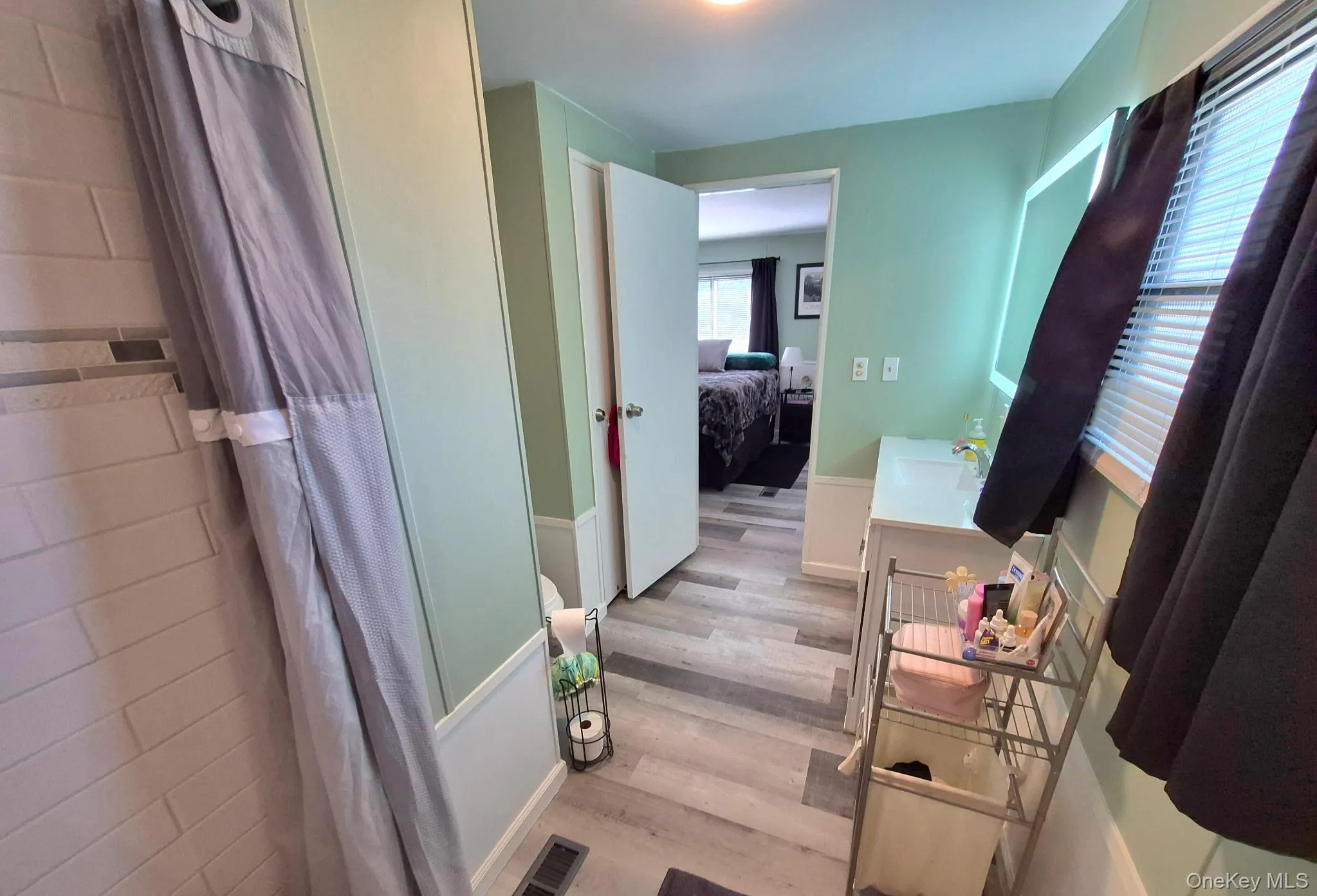 Full bathroom featuring wood-finish flooring, white subway tile shower surround, and a vanity with a rectangular basin Full bathroom featuring wood-finish flooring, white subway tile shower surround, and a vanity with a rectangular basin