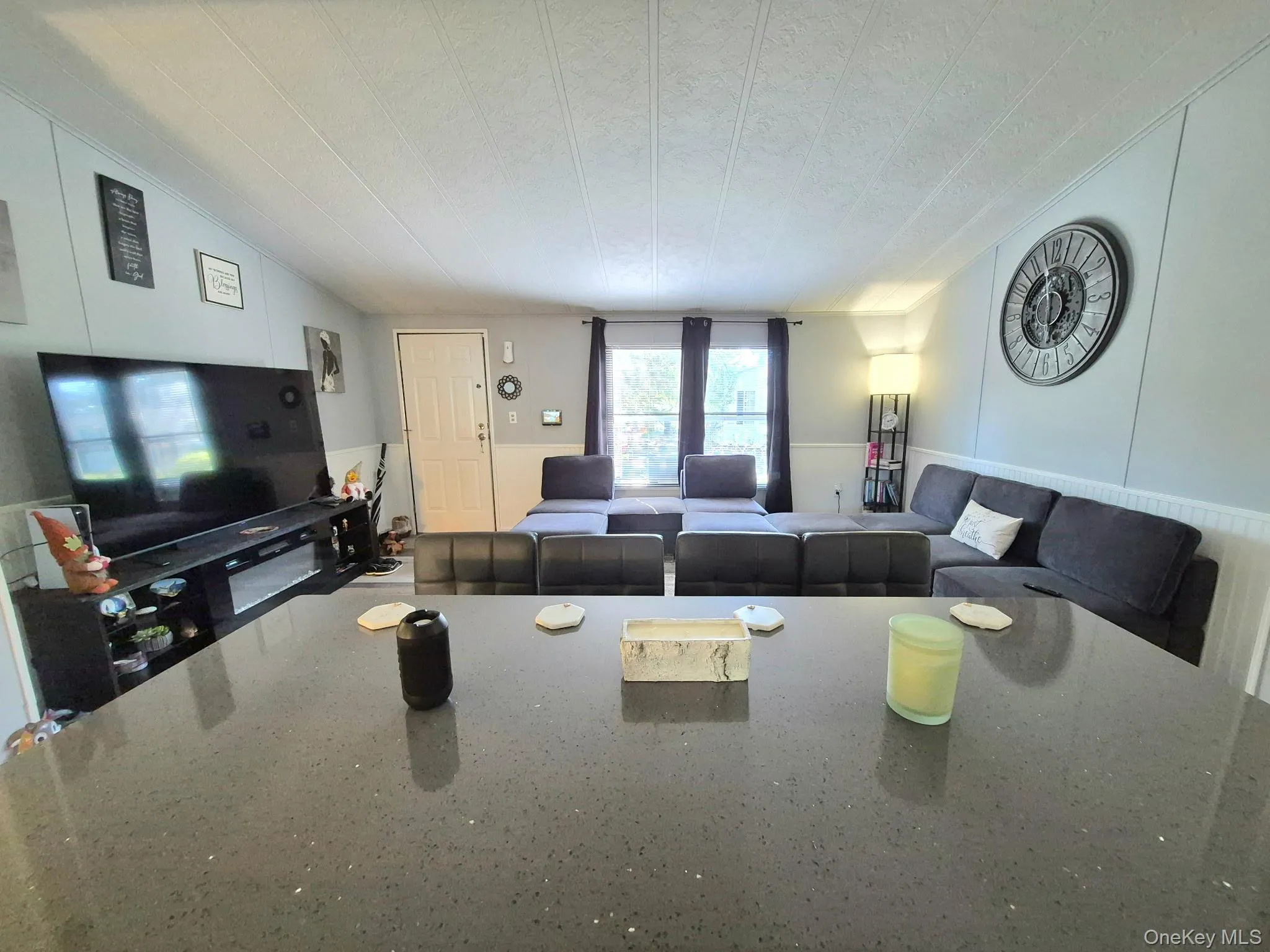 Spacious living area featuring a large window, paneling, and a textured ceiling Spacious living area featuring a large window, paneling, and a textured ceiling