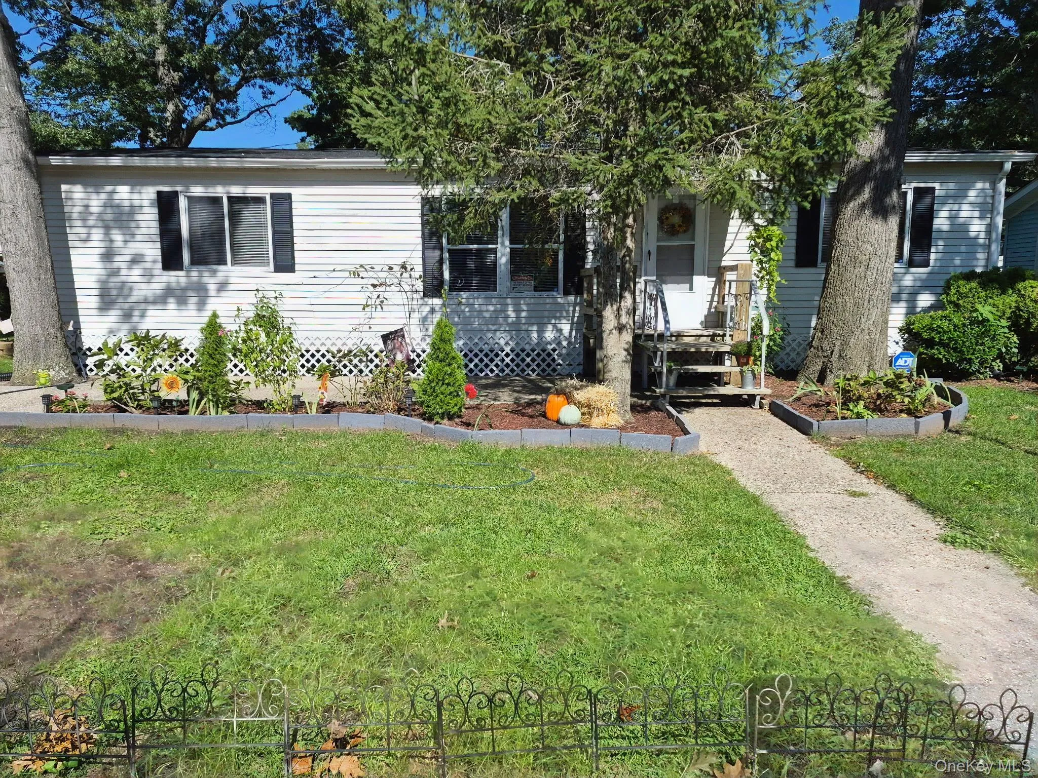 White siding exterior with black shutters, front porch with railing, concrete walkway, and landscaped front yard with mature trees White siding exterior with black shutters, front porch with railing, concrete walkway, and landscaped front yard with mature trees