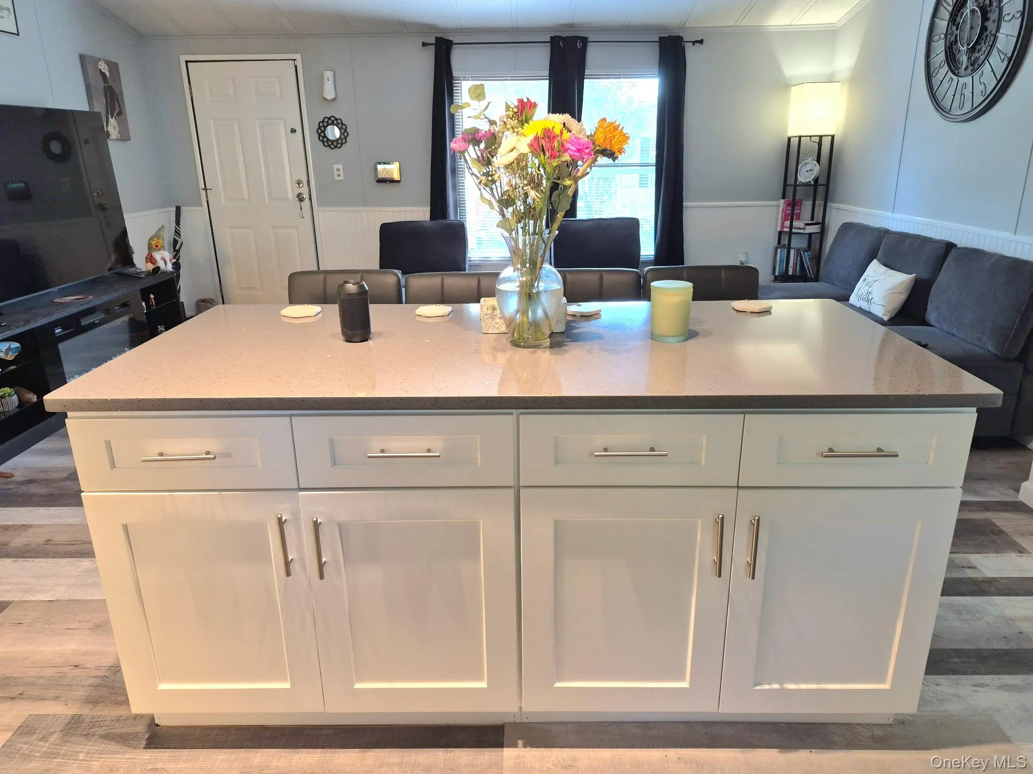 Kitchen island with light-toned countertop, white cabinetry with silver-tone hardware, and wood-finish flooring Kitchen island with light-toned countertop, white cabinetry with silver-tone hardware, and wood-finish flooring