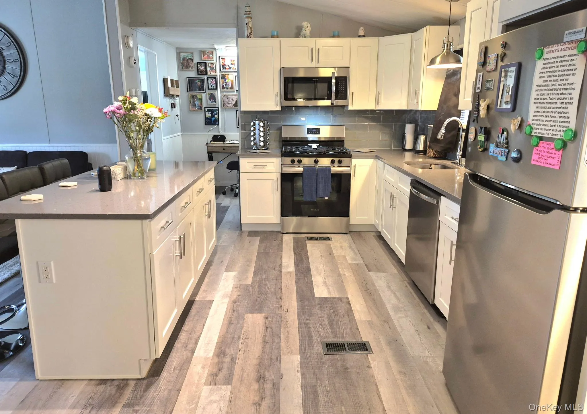 Full kitchen featuring white cabinetry, stainless steel appliances, wood-finish flooring, and a large kitchen island with a light-toned countertop Full kitchen featuring white cabinetry, stainless steel appliances, wood-finish flooring, and a large kitchen island with a light-toned countertop