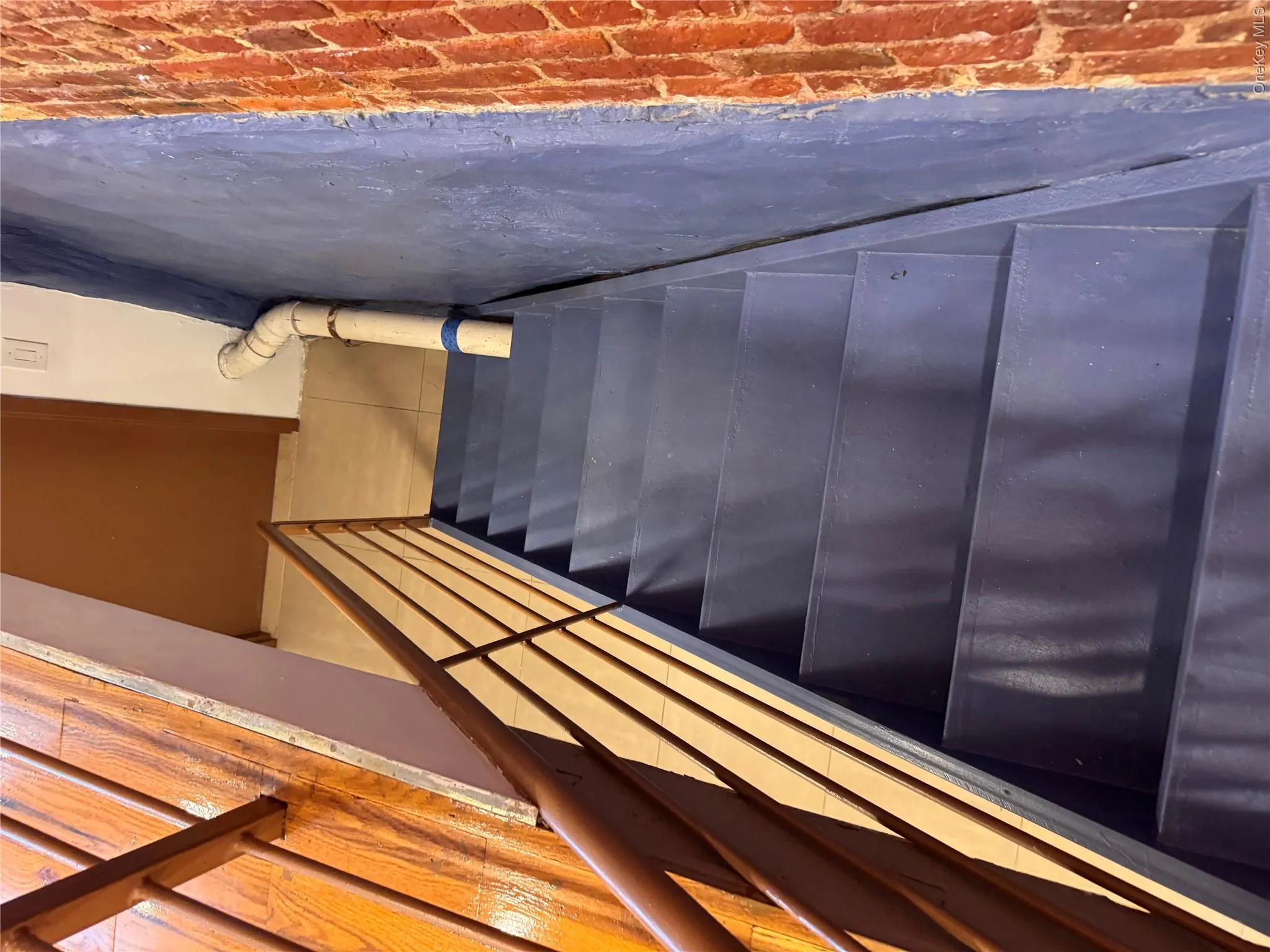 Staircase with painted treads, wood-finish handrail, and exposed brick wall Staircase with painted treads, wood-finish handrail, and exposed brick wall