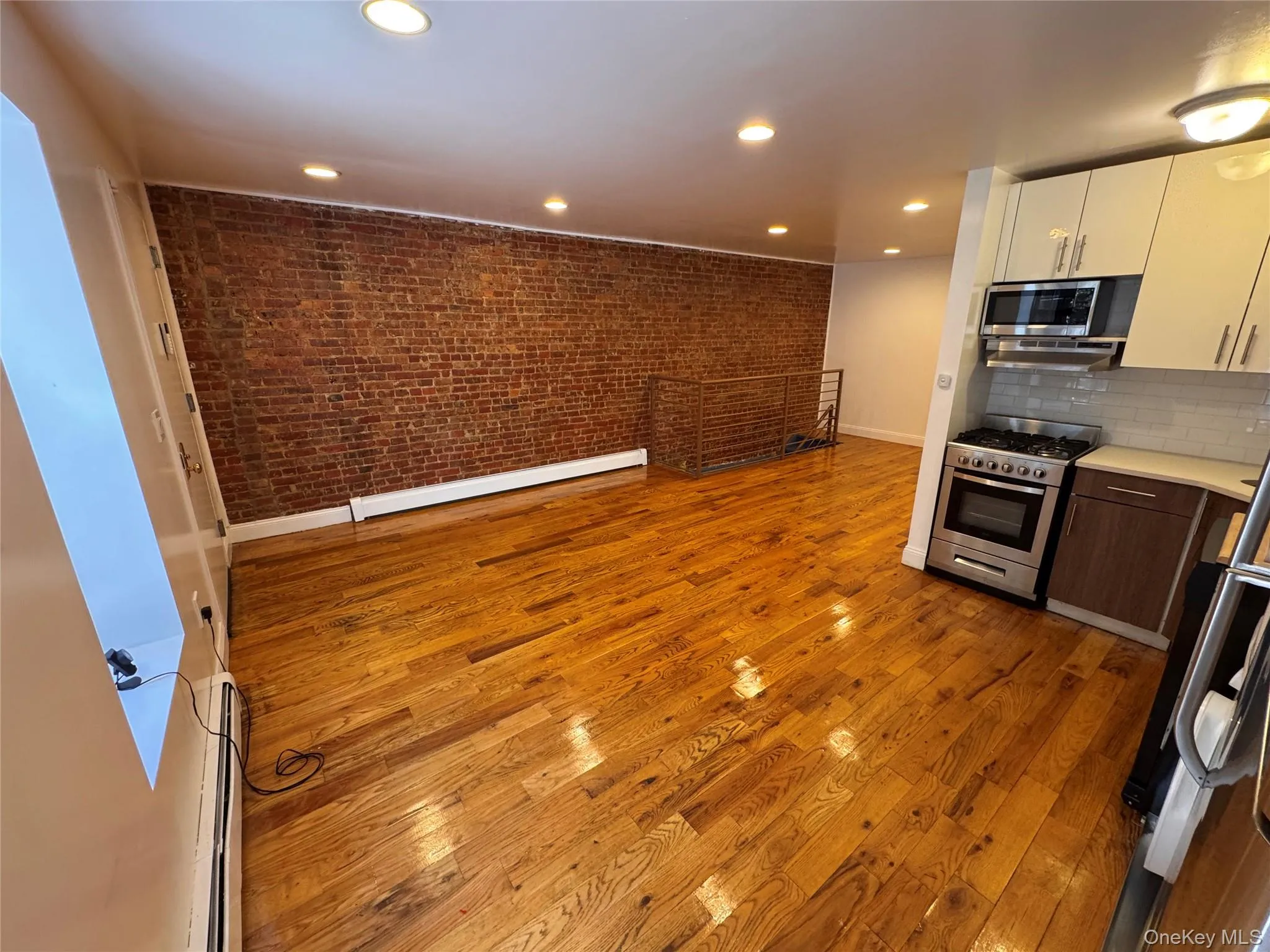 Hardwood flooring, exposed brick wall, recessed lighting, stainless steel appliances, and white shaker-style cabinetry Hardwood flooring, exposed brick wall, recessed lighting, stainless steel appliances, and white shaker-style cabinetry