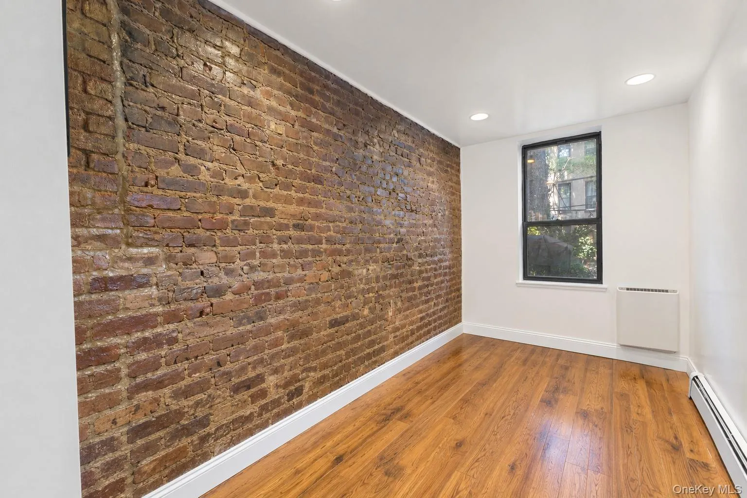 Bedroom 2 with exposed brick wall, wood-finish flooring, recessed lighting, and a single window with dark trim Bedroom 2 with exposed brick wall, wood-finish flooring, recessed lighting, and a single window with dark trim